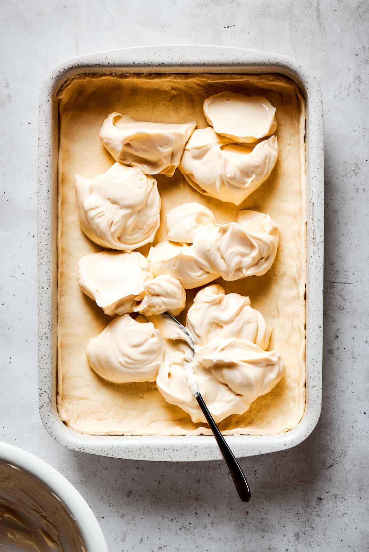 Cream cheese filling scooped into a baking dish.