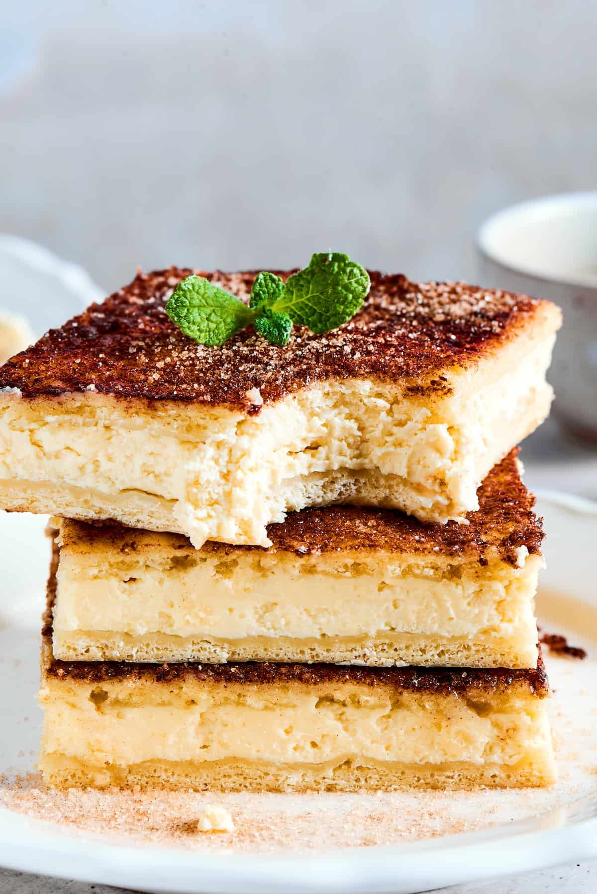Three squares of sopapilla cheesecake stacked on a plate. One has had a bite taken from it.