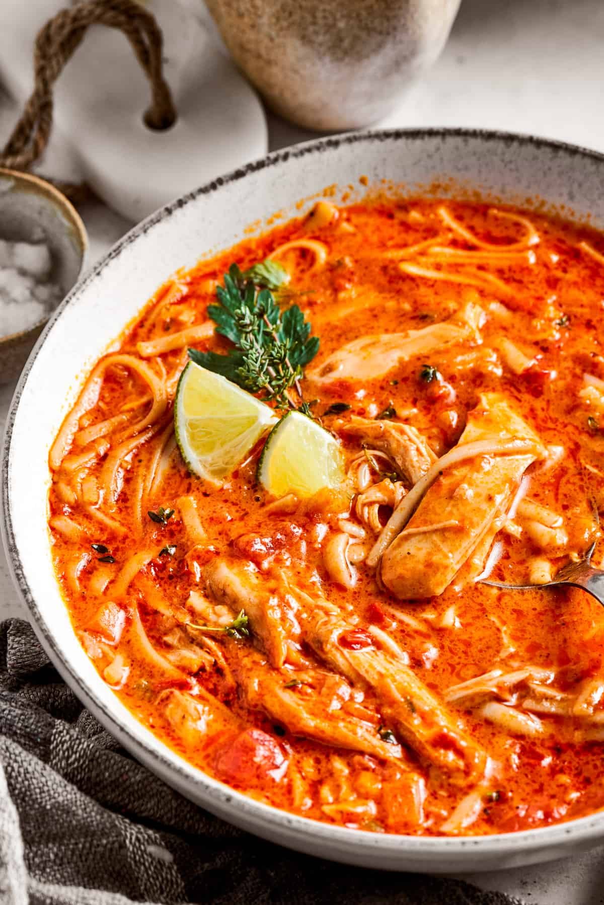 Close-up image of spicy chicken soup served in a bowl and garnished with lime wedges.