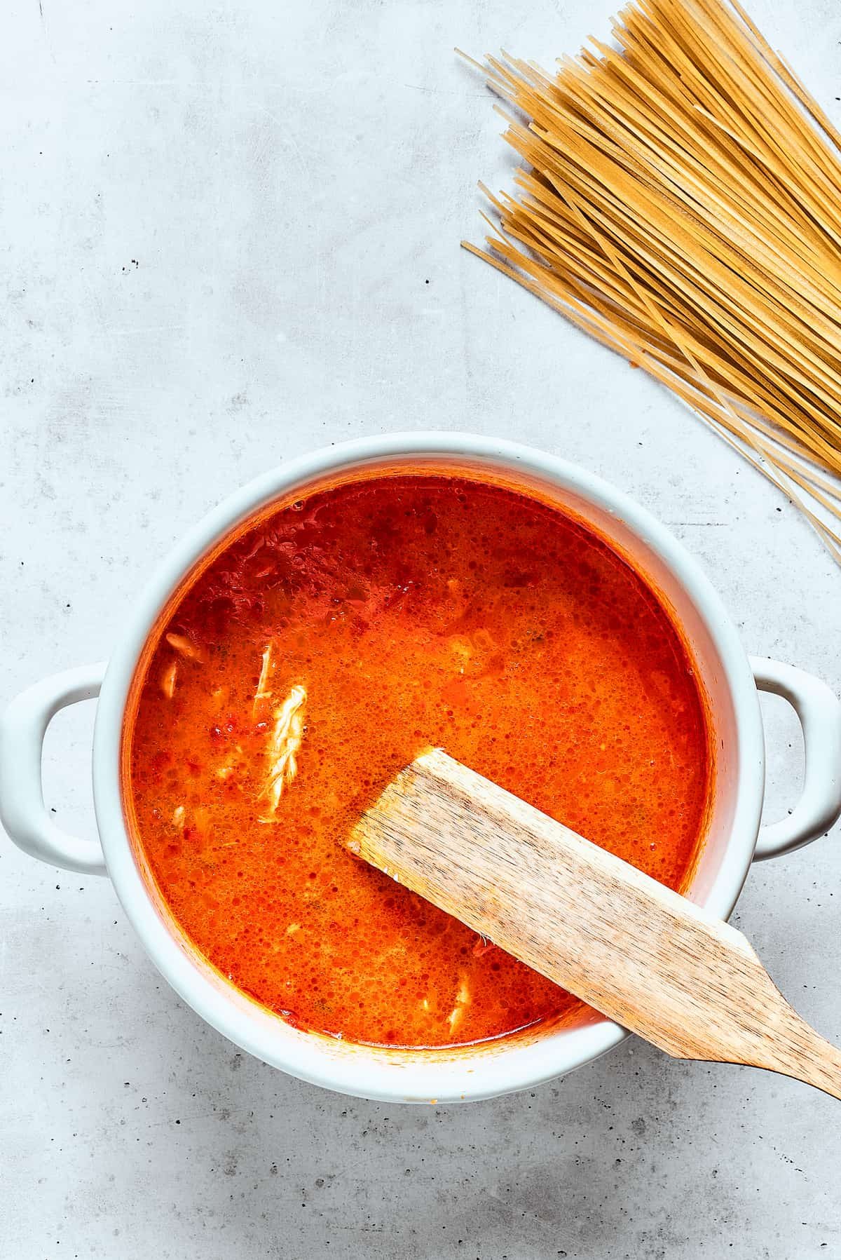 Noodles are added to spicy chicken soup with more noodles nearby.