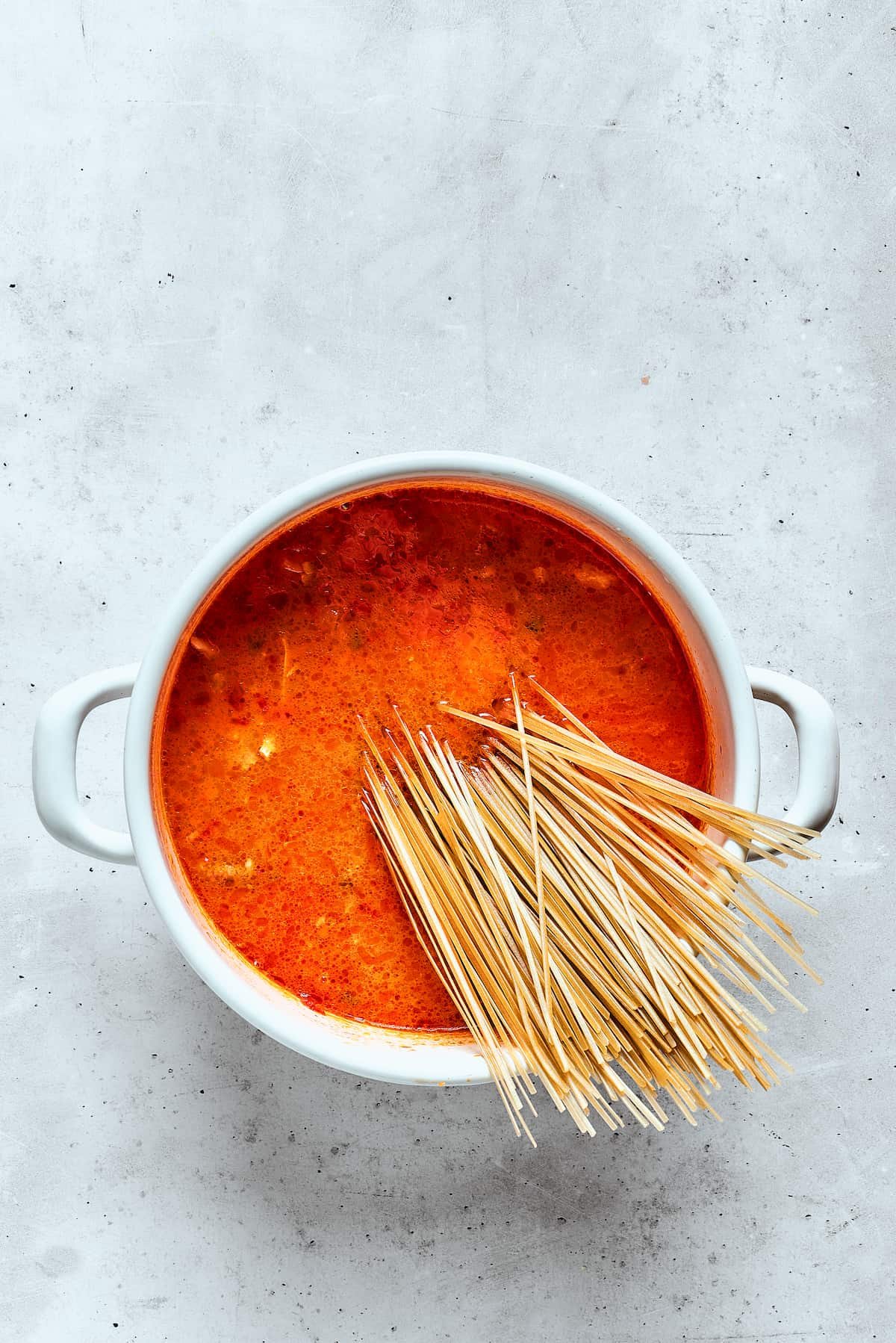 Rice noodles are added to a pot of spicy chicken soup.
