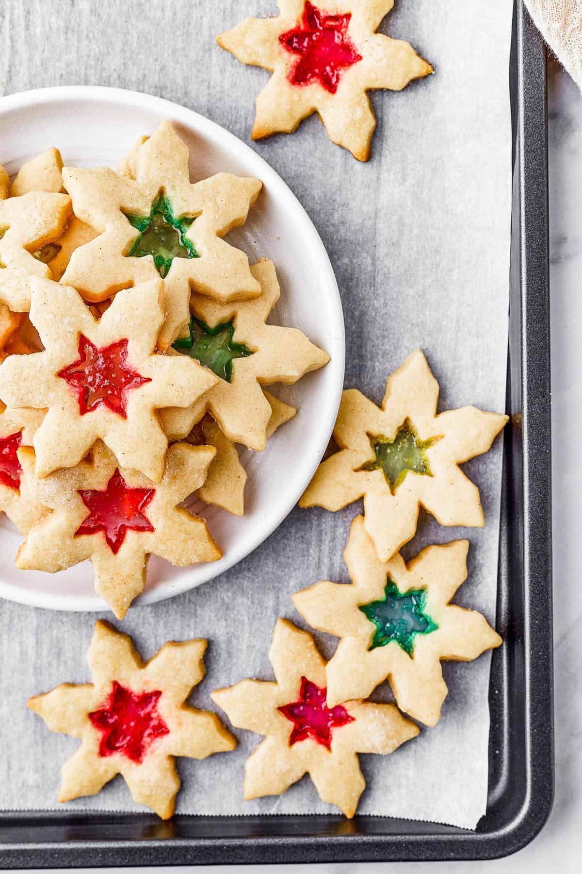 Two plates of stained glass cookies, with extra cookies arranged artistically on the table, along with a glass of milk.