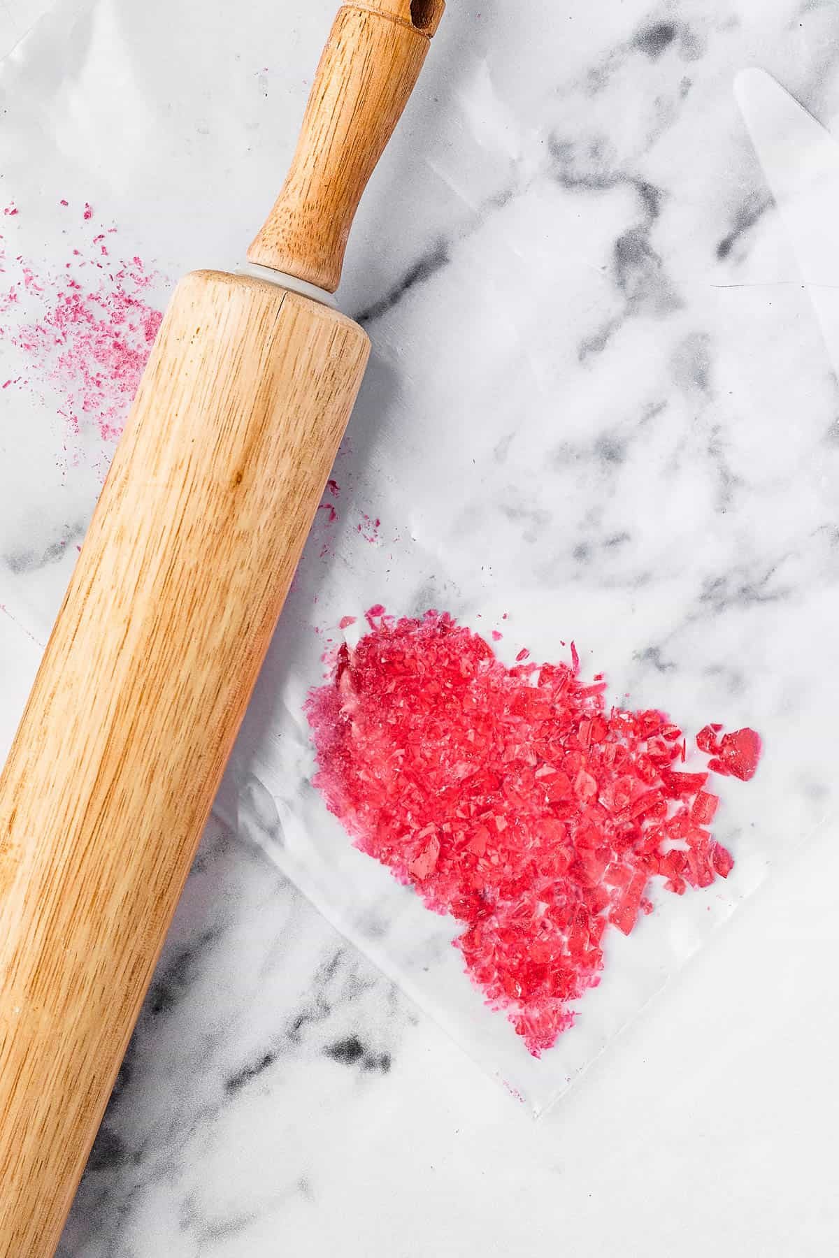 Hard candies crushed on a marble work surface. A rolling pin is on the surface next to the candies.