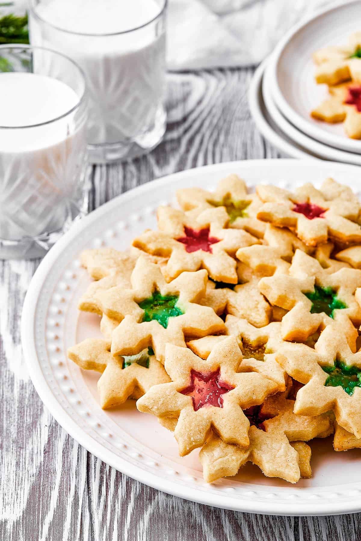 A platter of cookies with glasses of milk arranged around it. Two cookies are on a small serving plate.