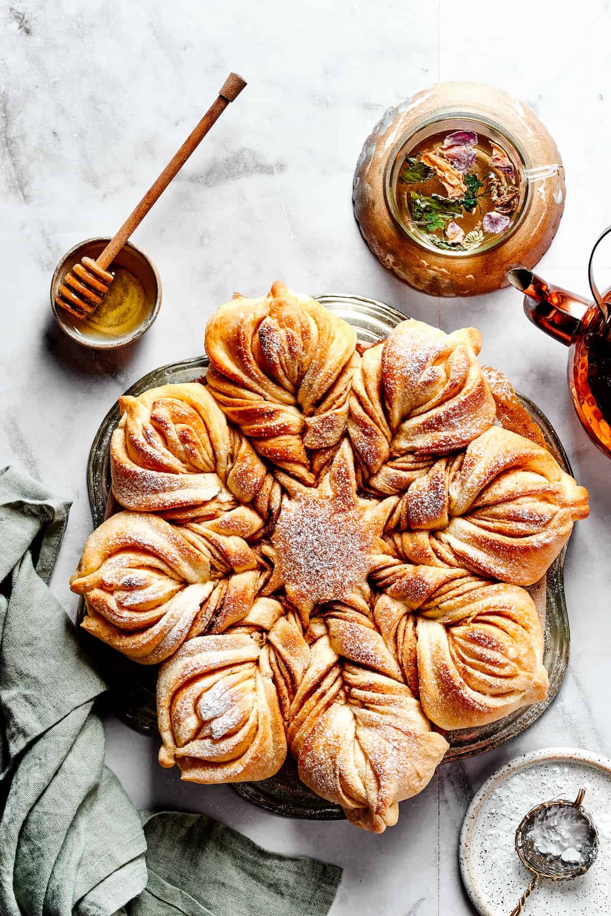 Overhead view of a star bread topped with powdered sugar, next to a bowl of honey.