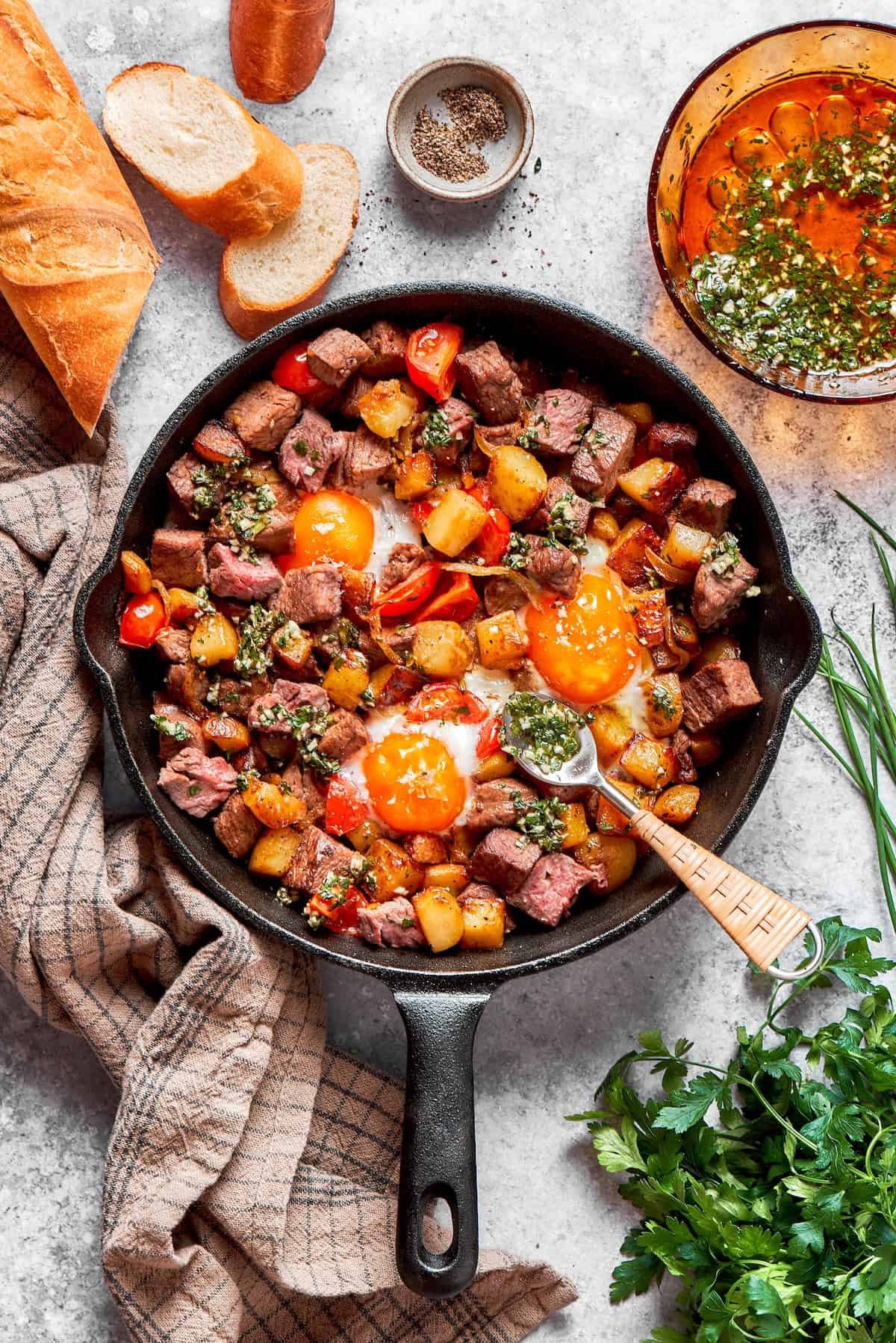 A cast iron skillet full of steak and eggs and a spoon.