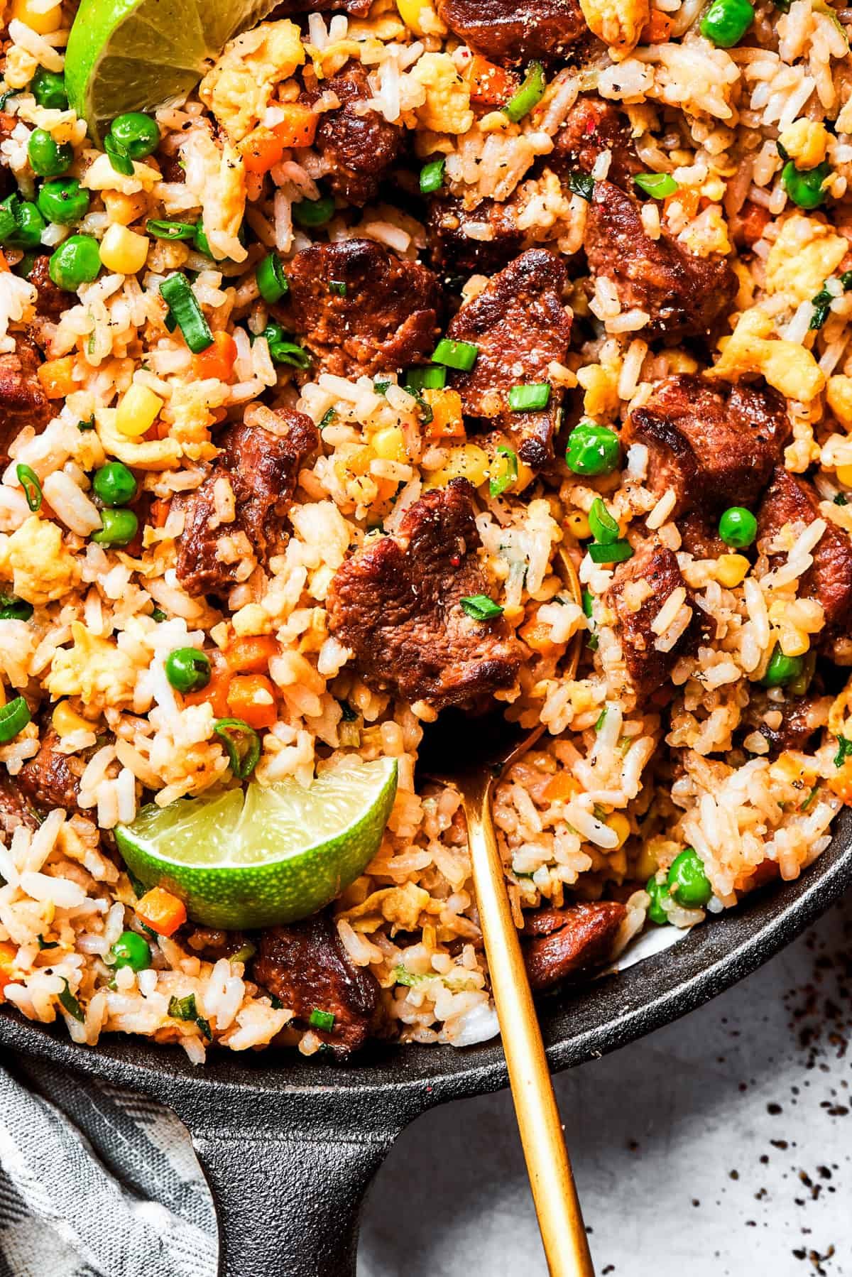 Stirring through steak fried rice garnished with lime wedges and green onions.