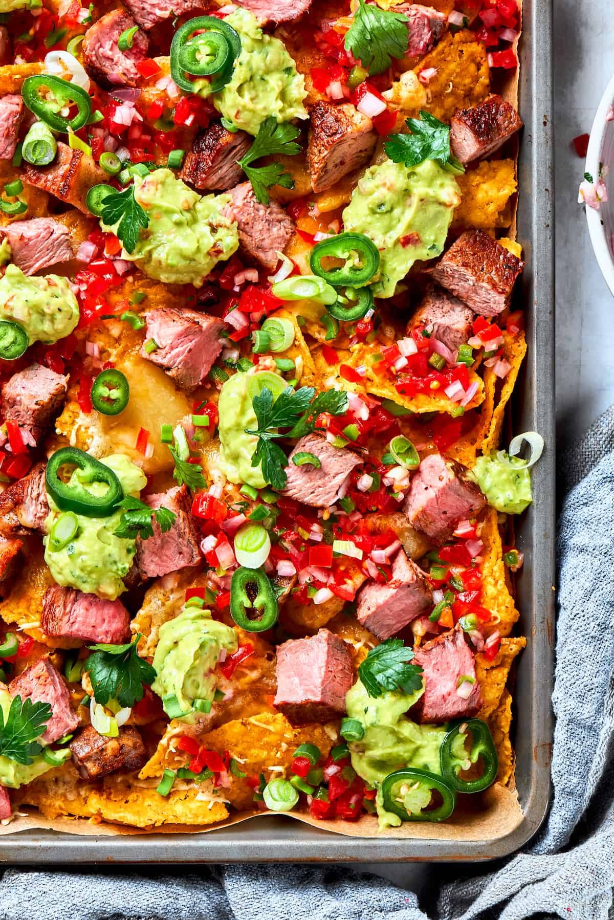 A big pan of steak nachos topped with guacamole and pico de gallo.