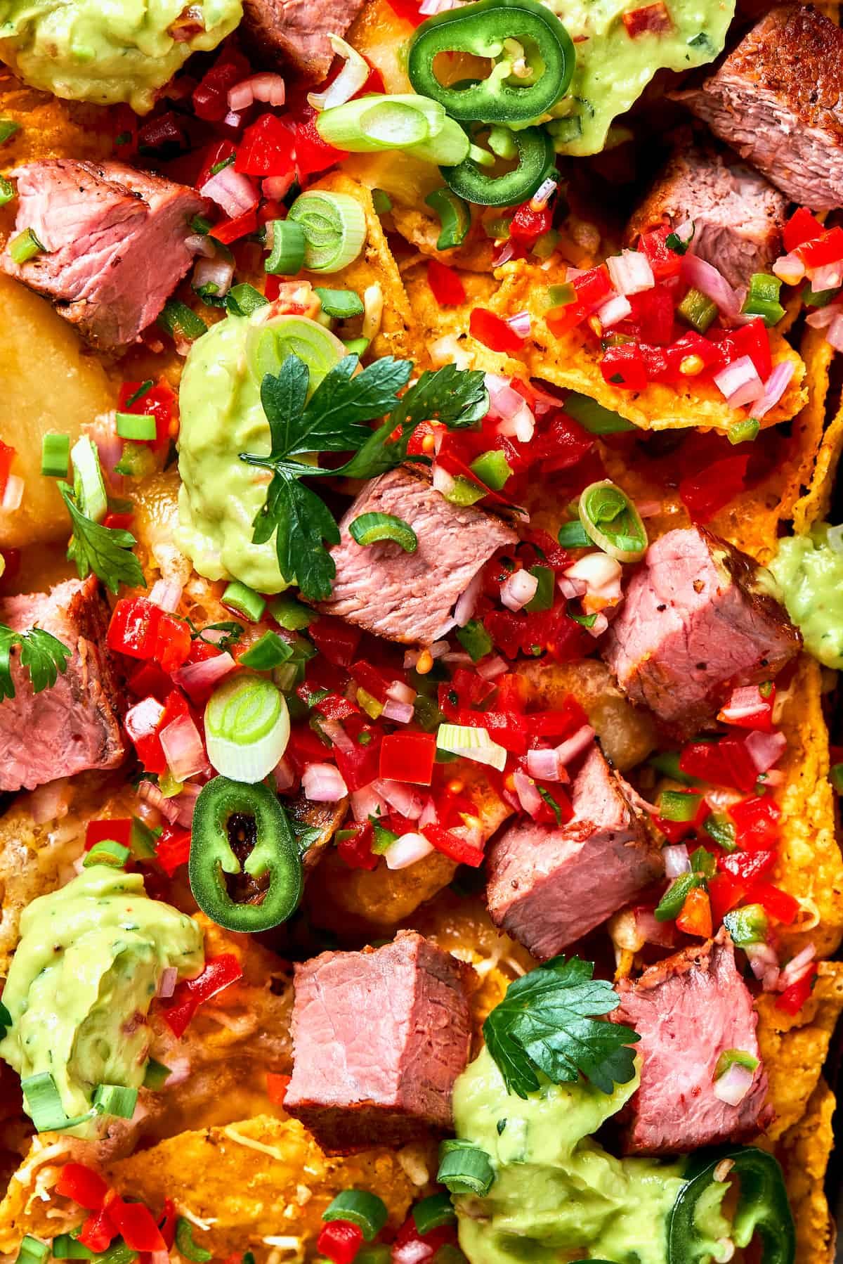Chunks of juicy steak and peppers top a pan of steak nachos.