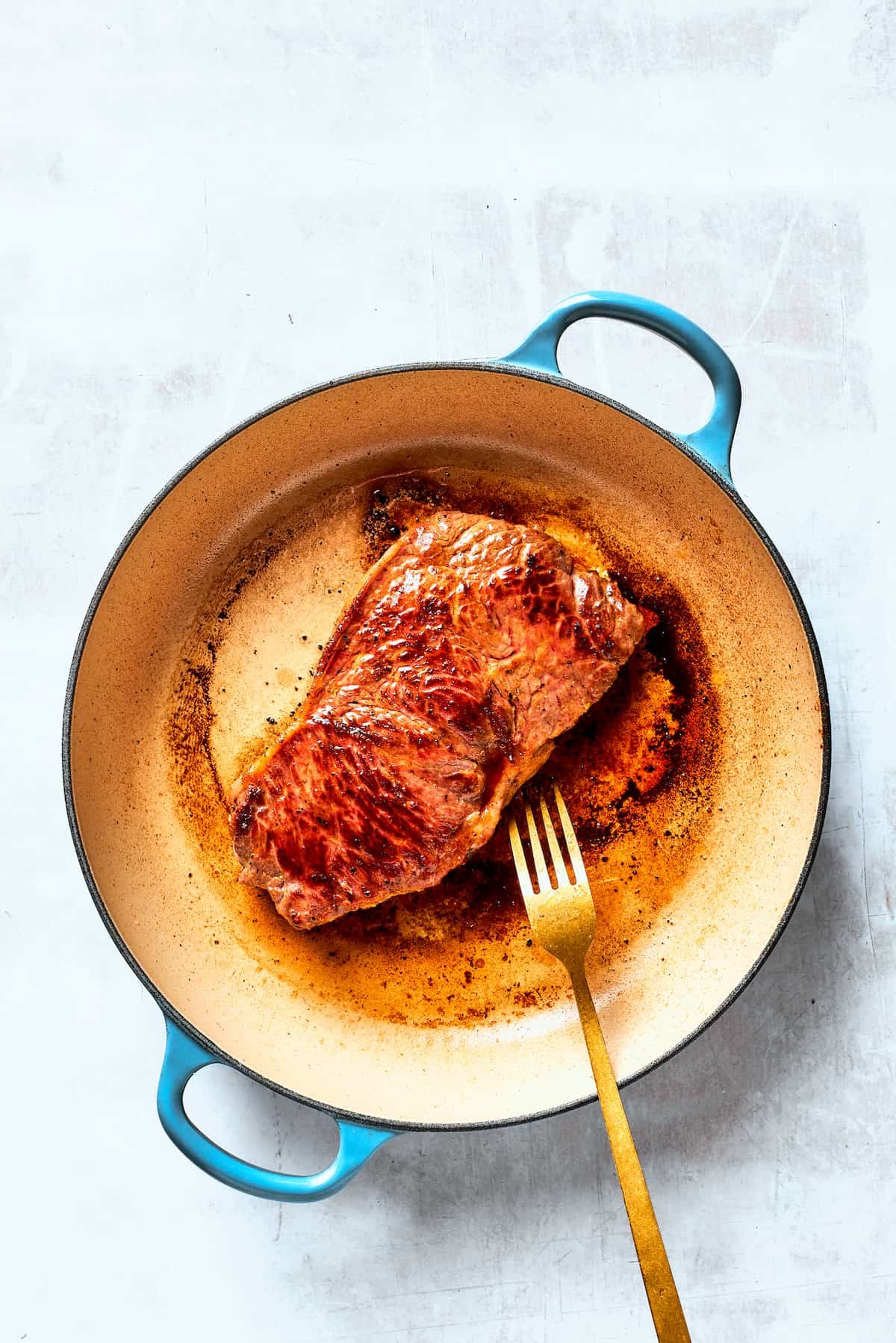 Steak is seared in a baking pan with a fork turning one of the steaks.