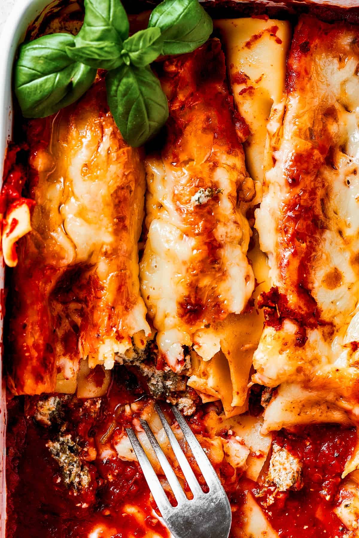 A casserole of baked pasta, with most of it removed from the dish, and a serving fork resting in the dish.