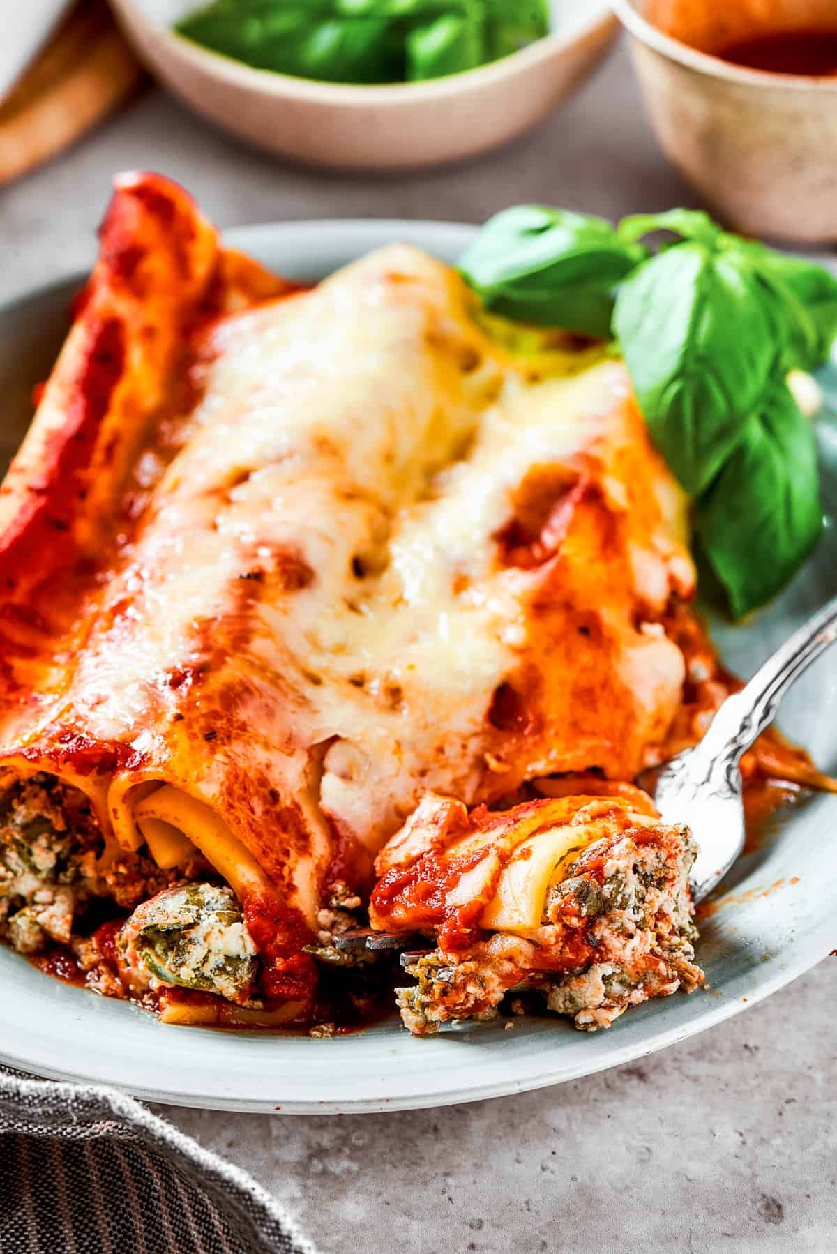A plate with three stuffed pasta tubes topped with melted cheese and herbs.