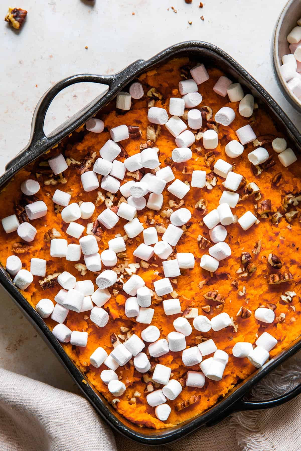 Close up shot of unbaked casserole, sprinkled with pecans and mini marshmallows.