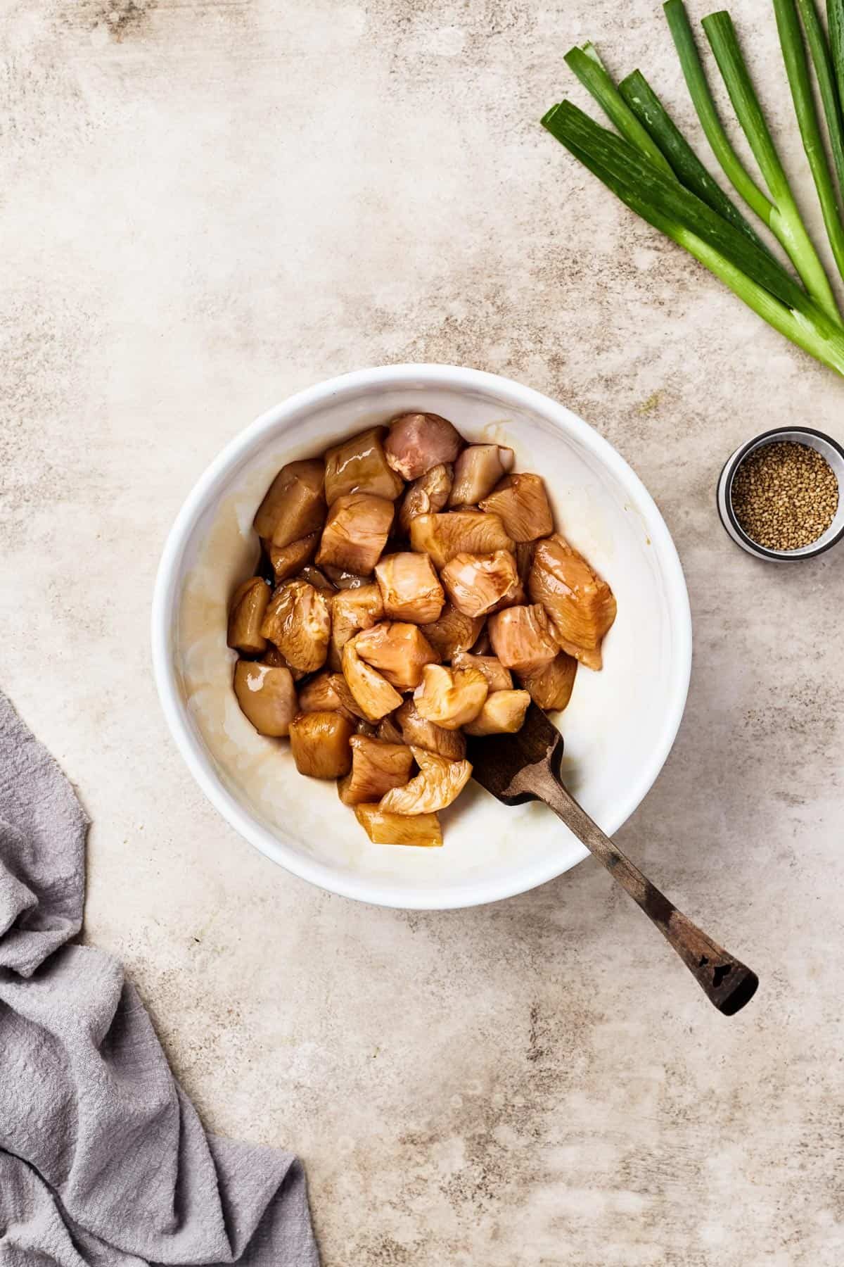 Chicken marinating in soy sauce in a white bowl.