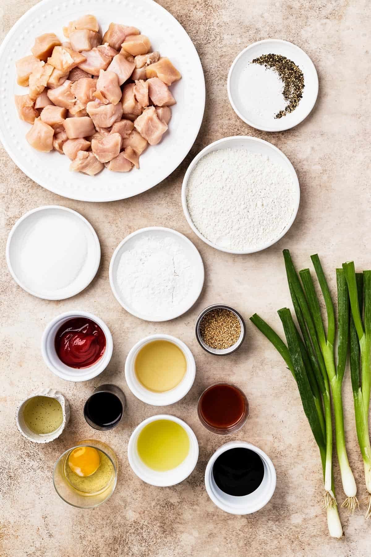 From top left: Chicken breast, salt and pepper, sugar, cornstarch, flour, ketchup, oil, toasted sesame seeds, rice vinegar, oyster sauce, sriracha, egg, pineapple juice, soy sauce, green onions.