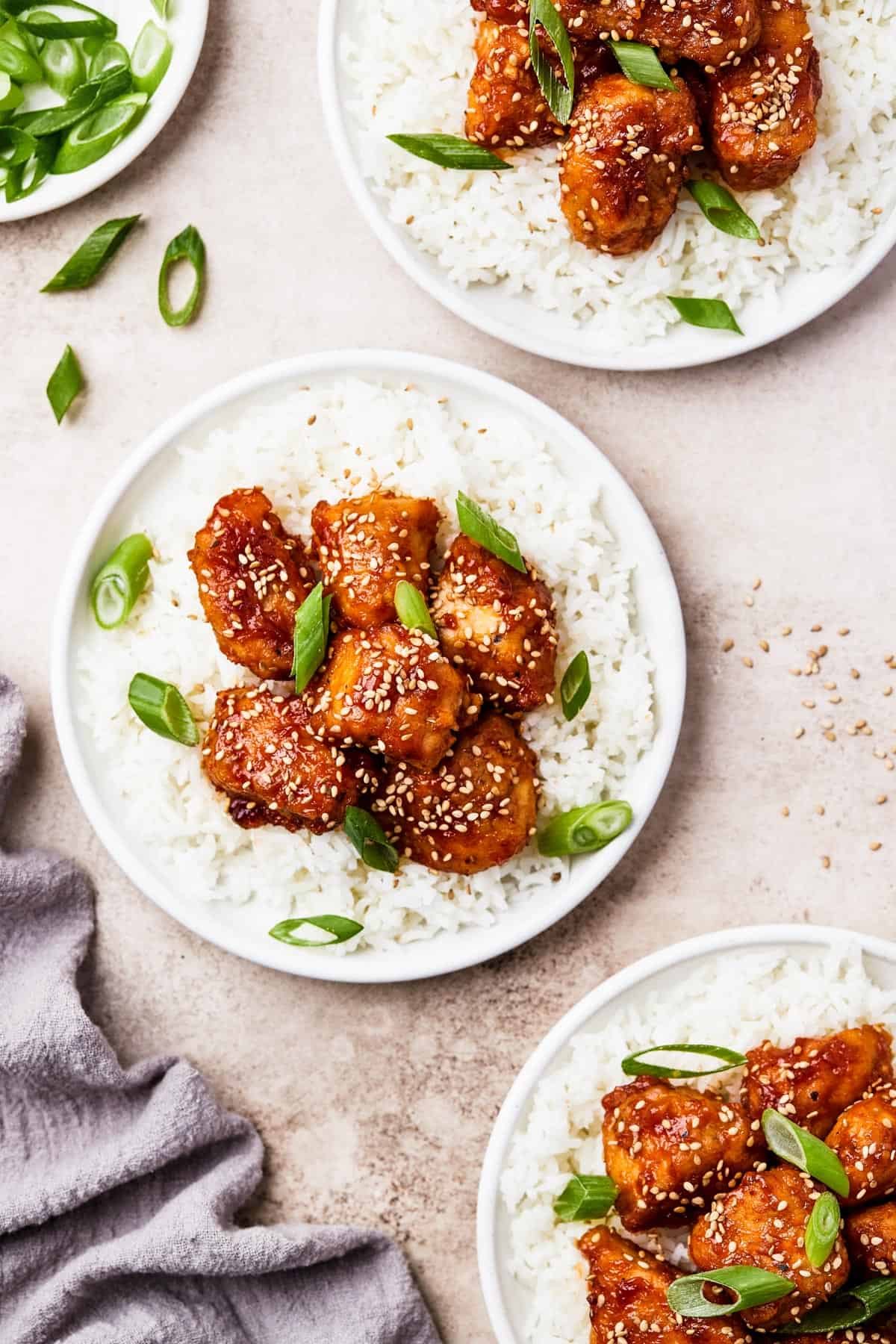 three plates topped with white rice topped with saucy chunks of chicken.