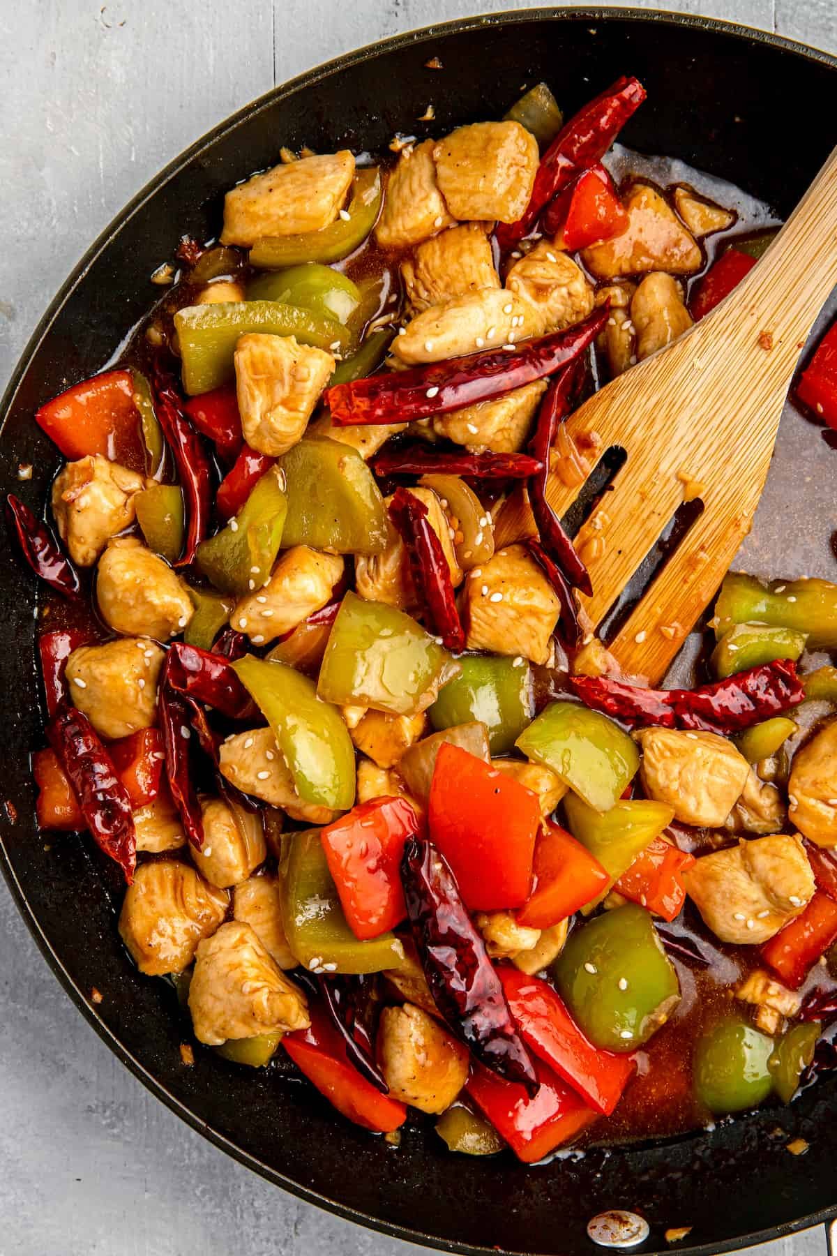 Szechuan chicken stir-fry in a cast-iron skillet with a wooden spatula.