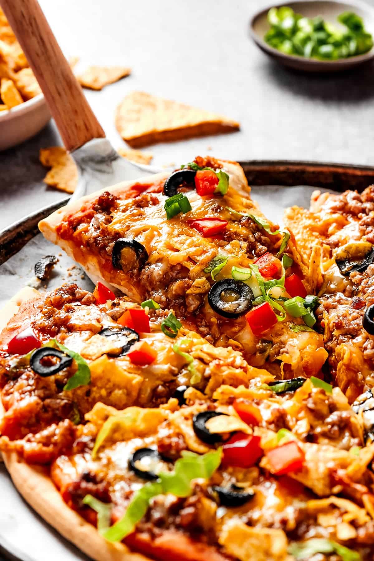 Lifting a slice of taco pizza with a pie server.