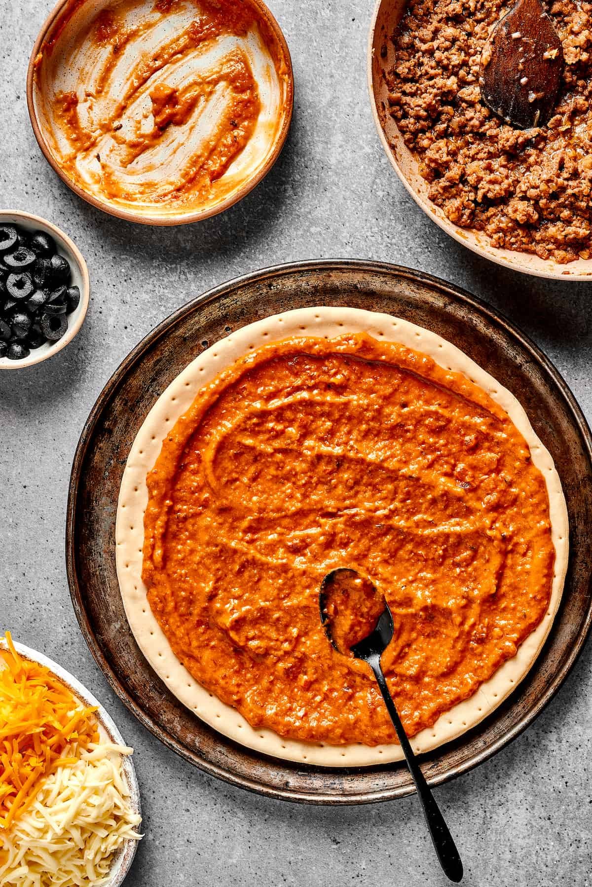Spreading refried bean sauce on a prepared pizza crust.