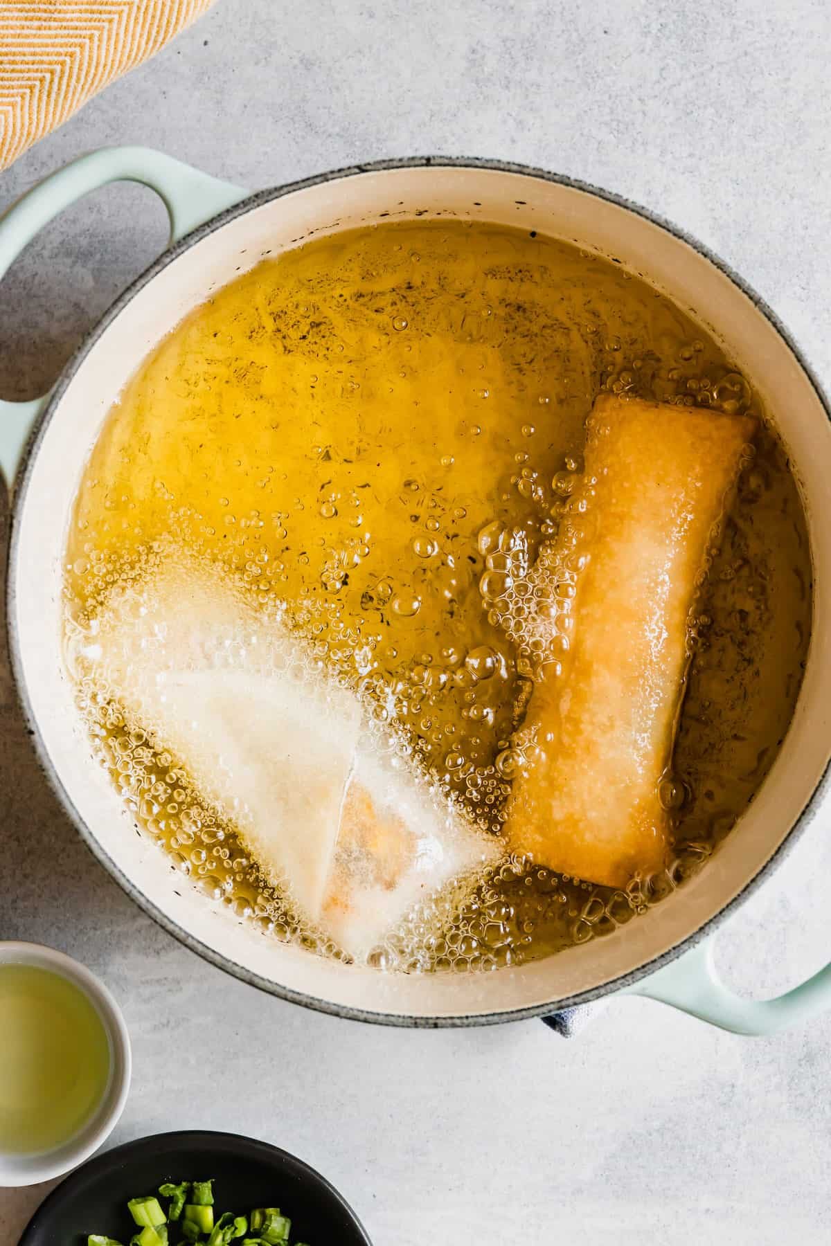 Two Egg Rolls Frying in a Double-Handle Pan with Oil