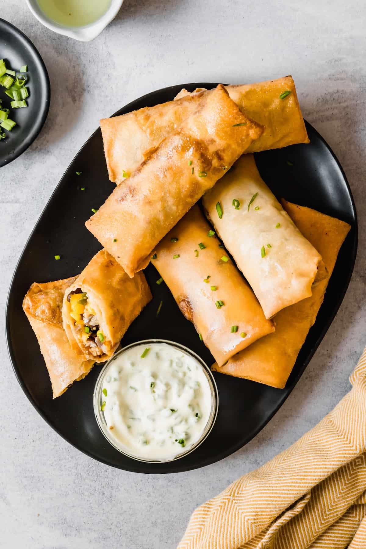 Homemade Egg Rolls on a Black Plate with a Container of Dipping Sauce