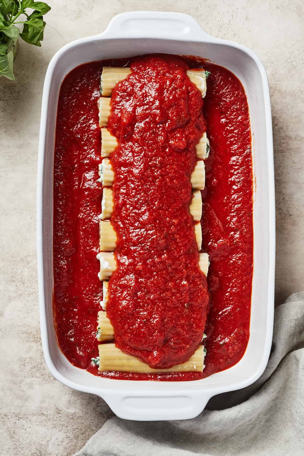 Uncooked pasta in a baking dish, covered in marinara.
