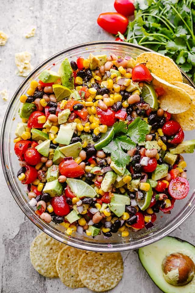 Cowboy caviar with avocado, corn, tomatoes, black-eyed peas, beans and cilantro in a large glass bowl
