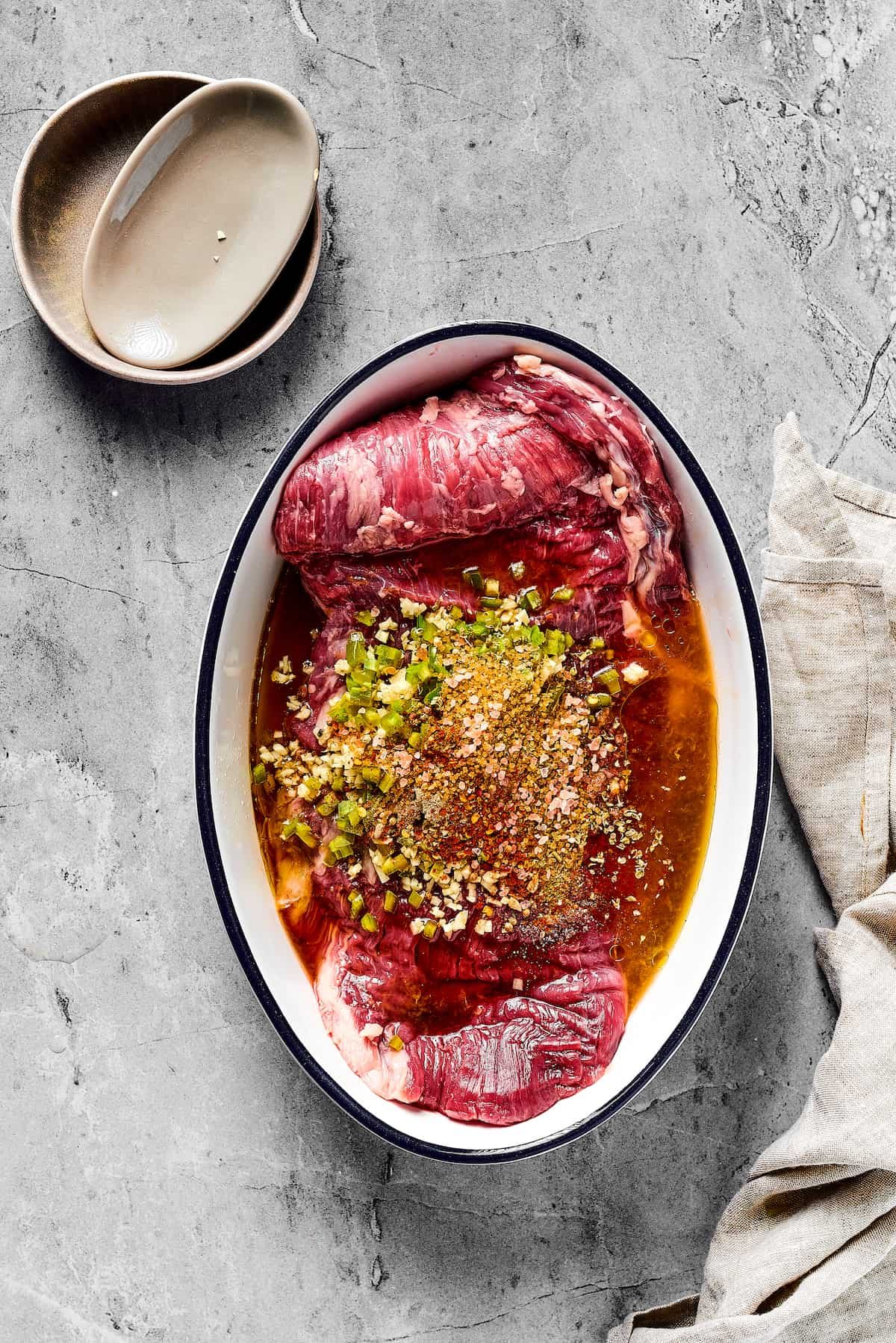 A flank steak in an enamel oval dish, covered in marinade.