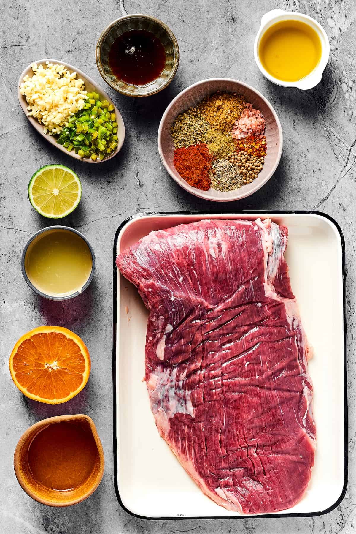 From top left: Minced garlic and jalapeno, maple syrup, spices, olive oil, lime juice, orange juice, flank steak.