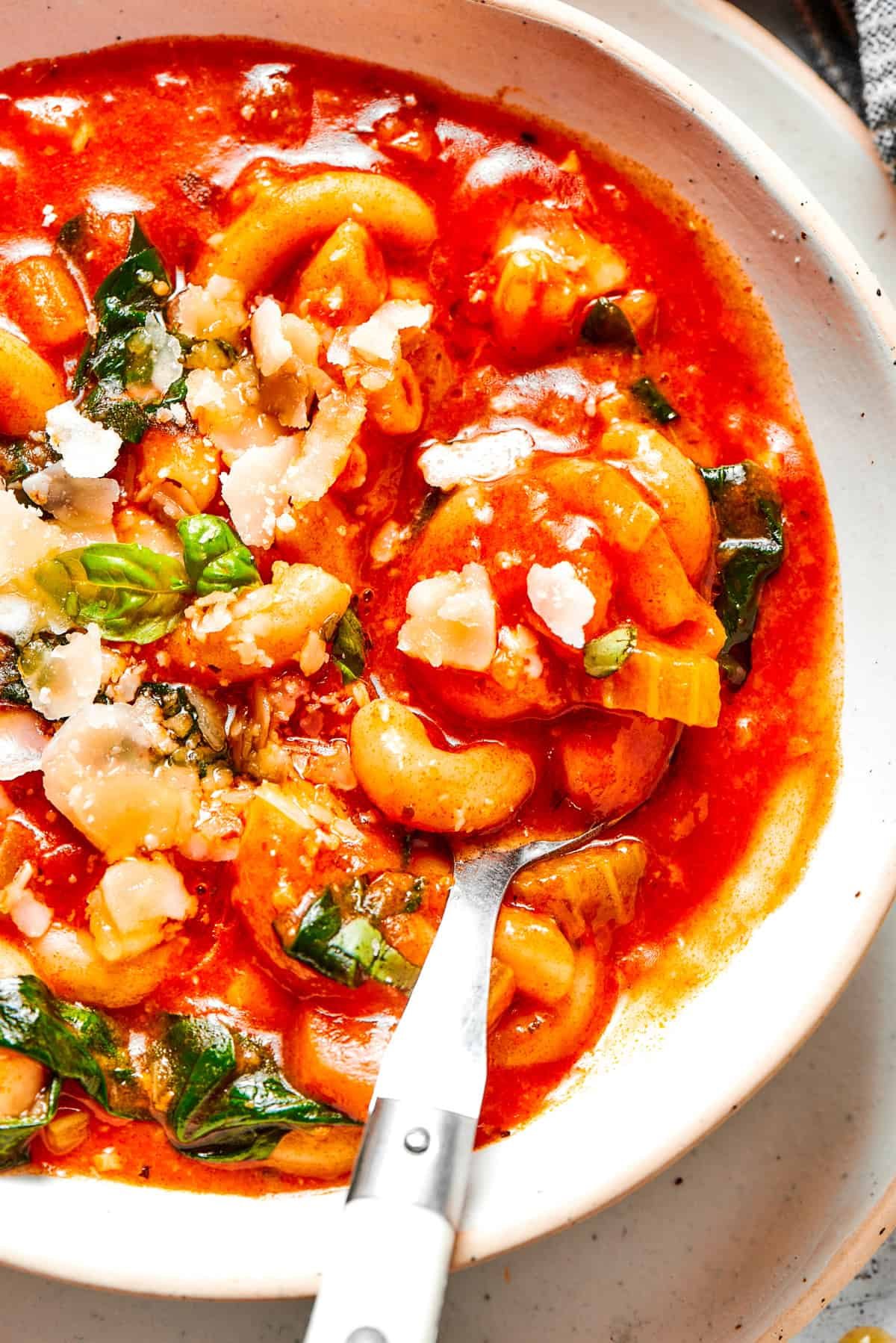Spoon stirring through tomato soup with spinach and pasta.