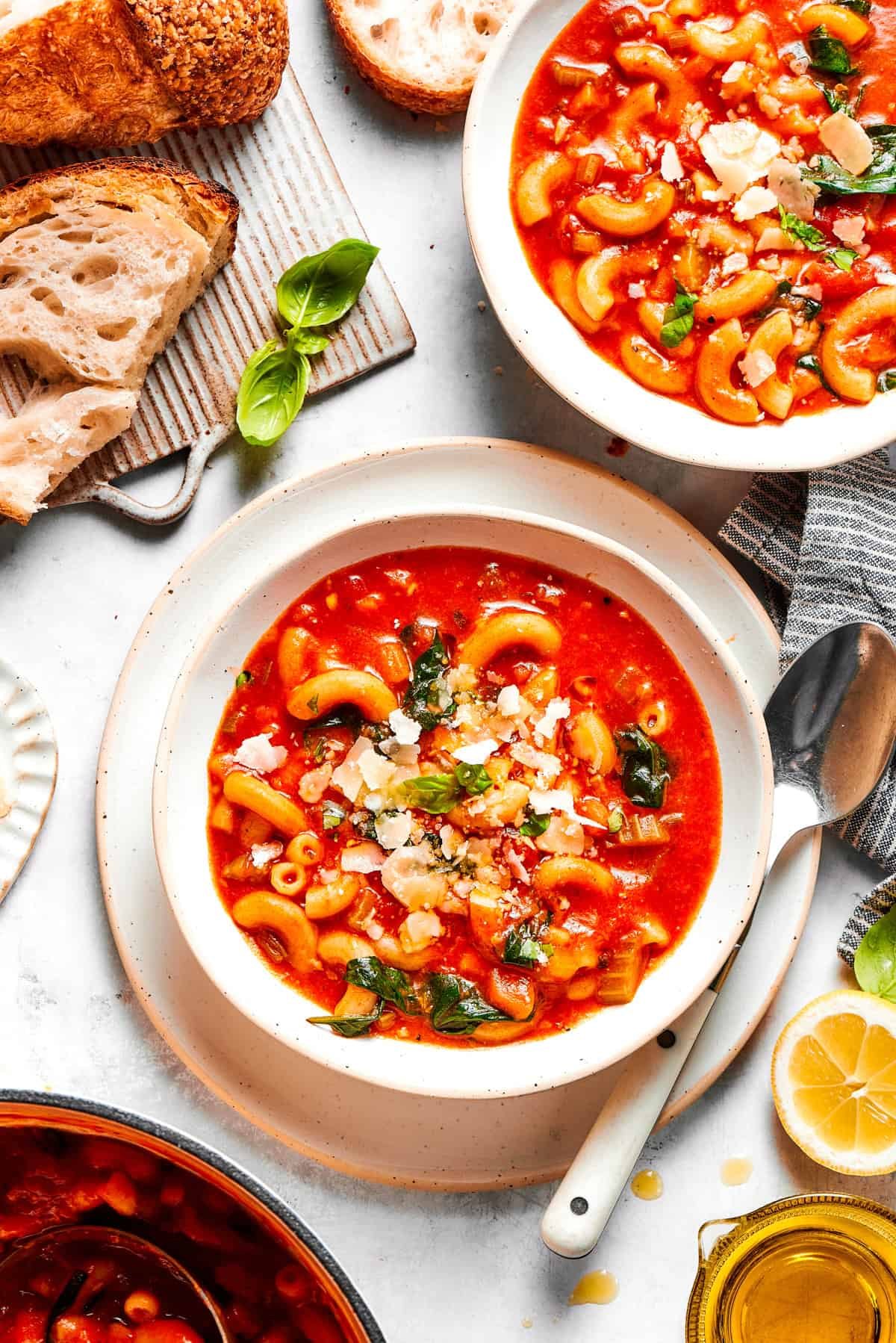 Two bowls of tomato soup, with bread and spoons placed near the bowls.