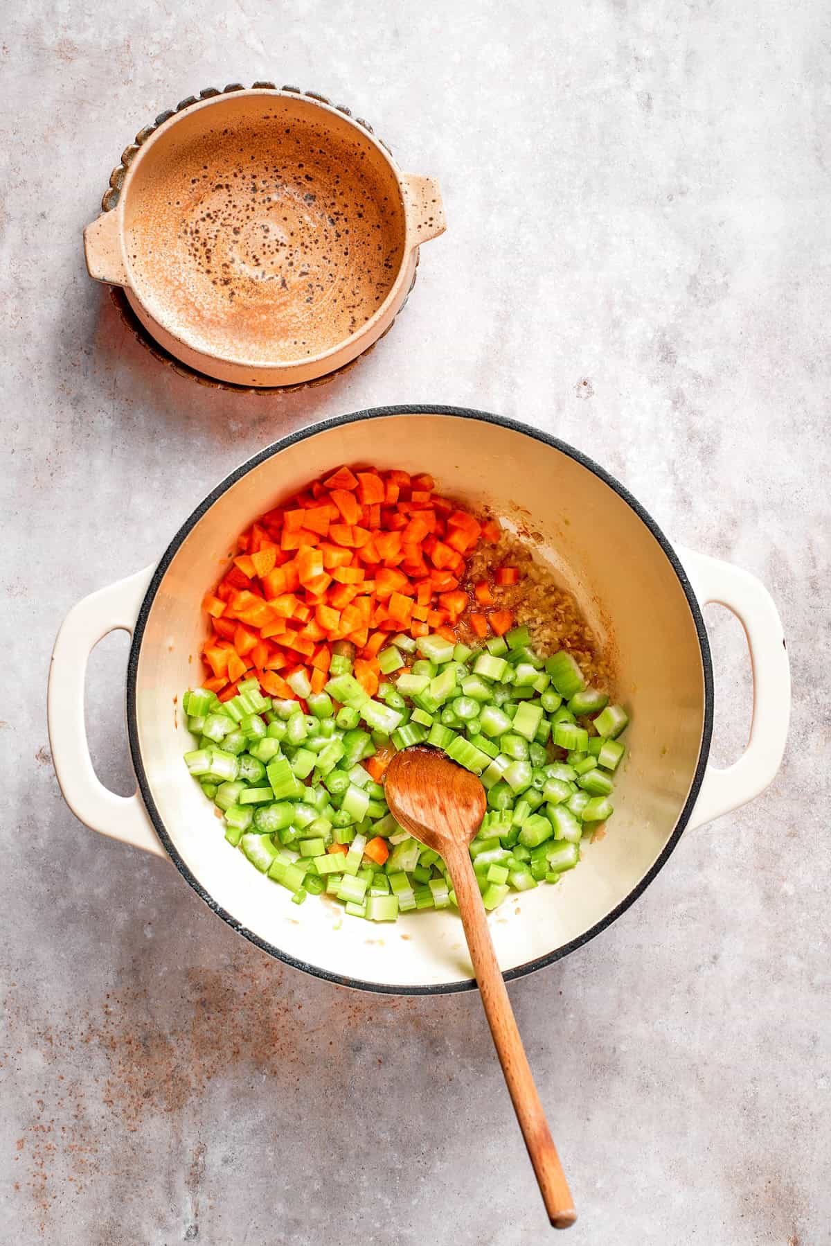 Celery and carrots are added to shallots in a pot.