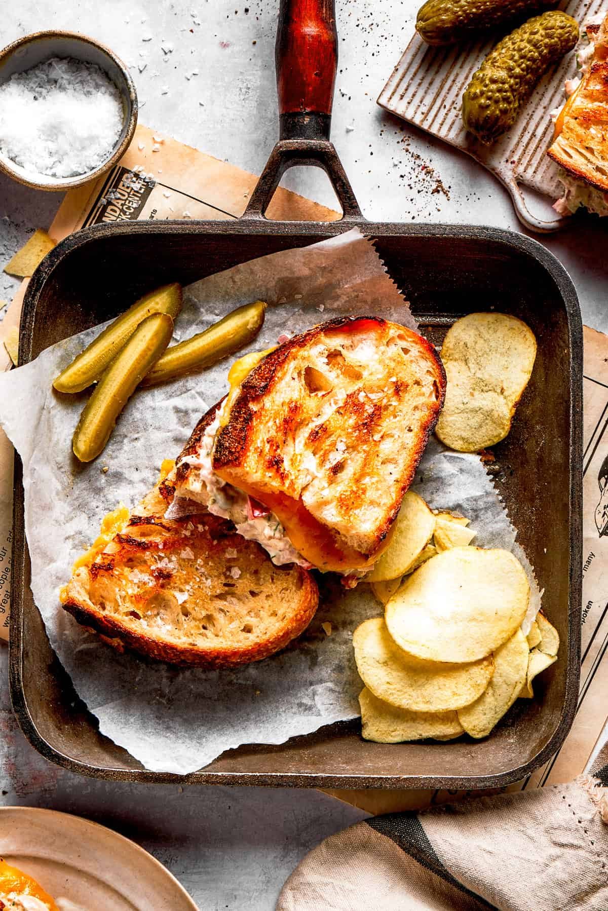 Two tuna melt sandwiches in a skillet with a pile of potato chips arranged next to them.