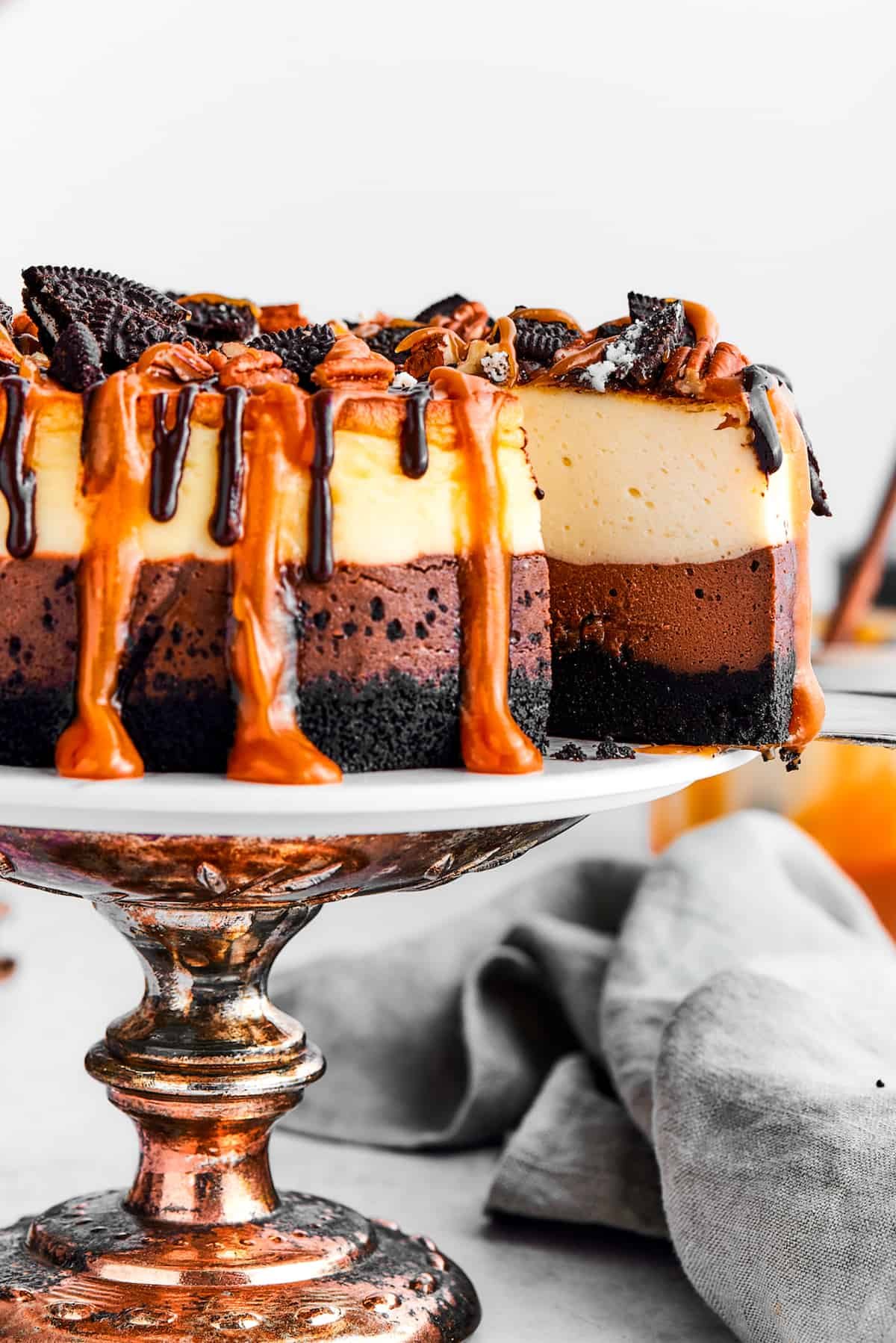 A slice of turtle cheesecake is slightly pulled out of the whole cheesecake on the cake stand.
