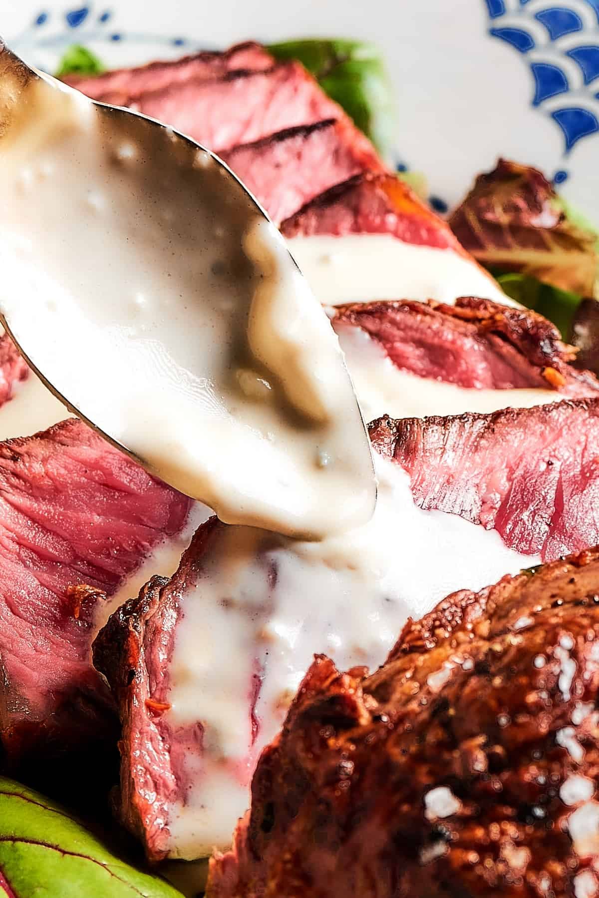 Steak slices with creamy sauce being spooned over the top.