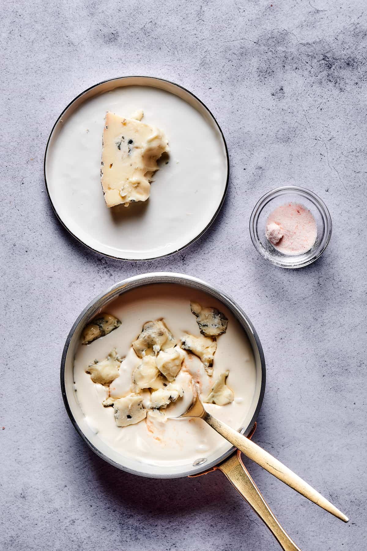 Chunks of blue cheese being stirred into a saucepan of creamy sauce.