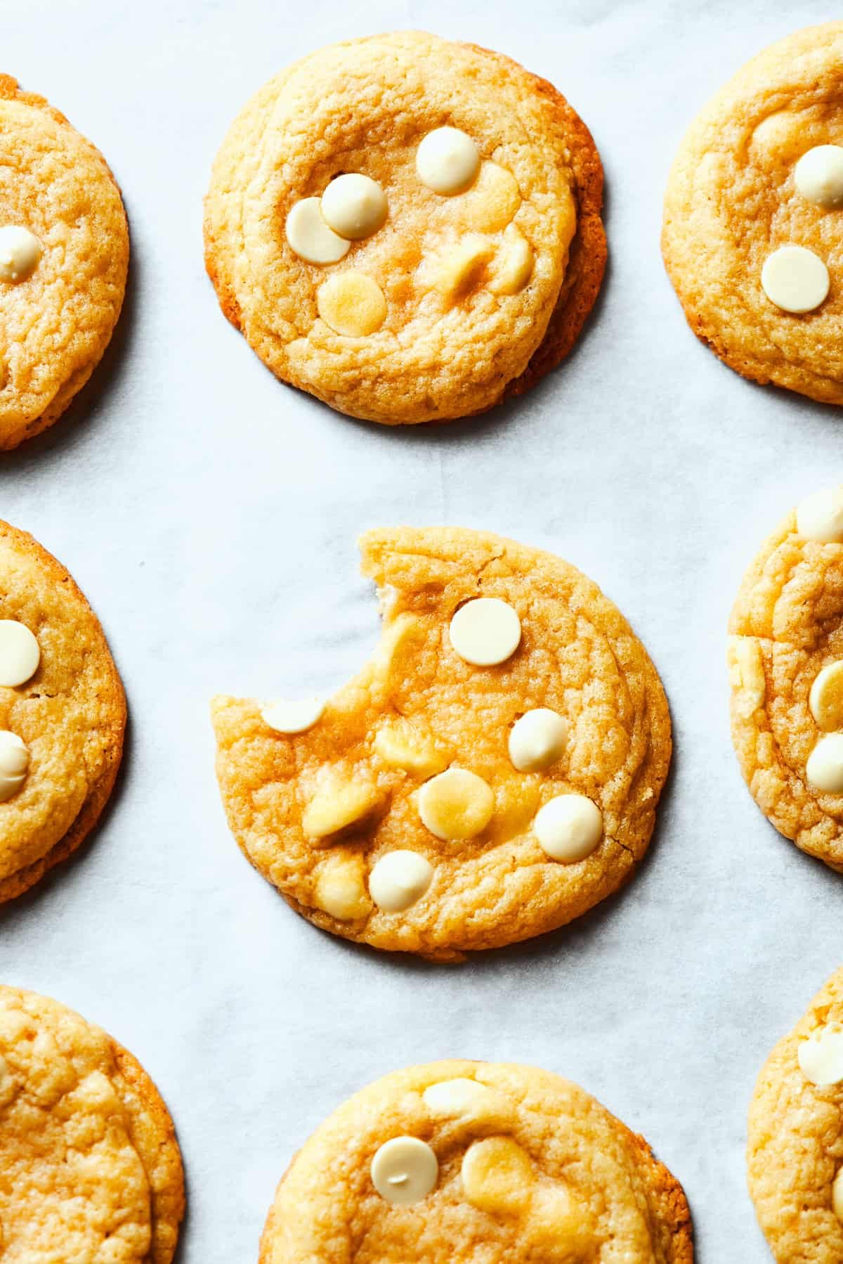 Chocolate chip cookies arranged on a white surface and the cookie in the center is missing a bite.