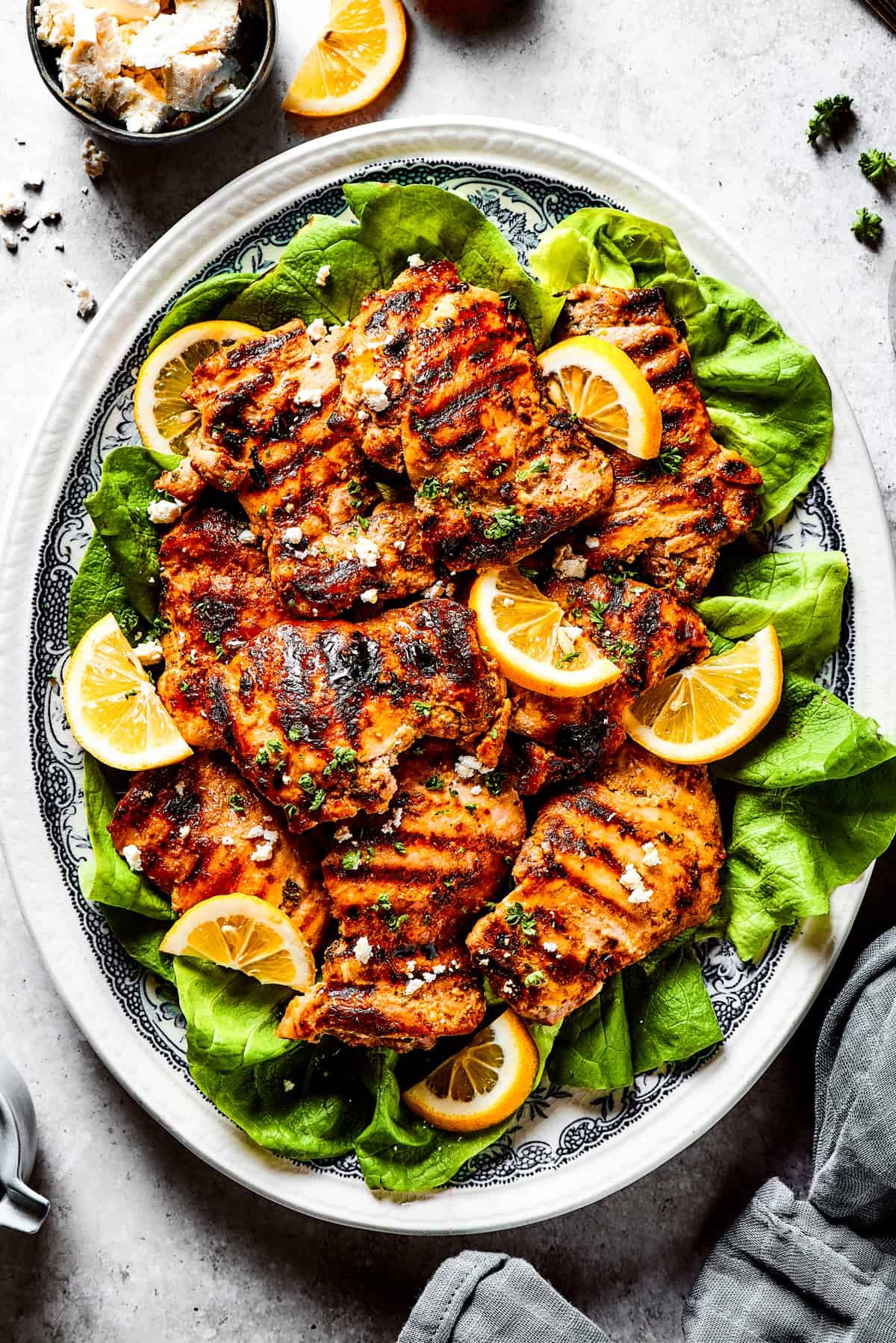 Grilled chicken thighs and lemon slices on a bed of salad greens.