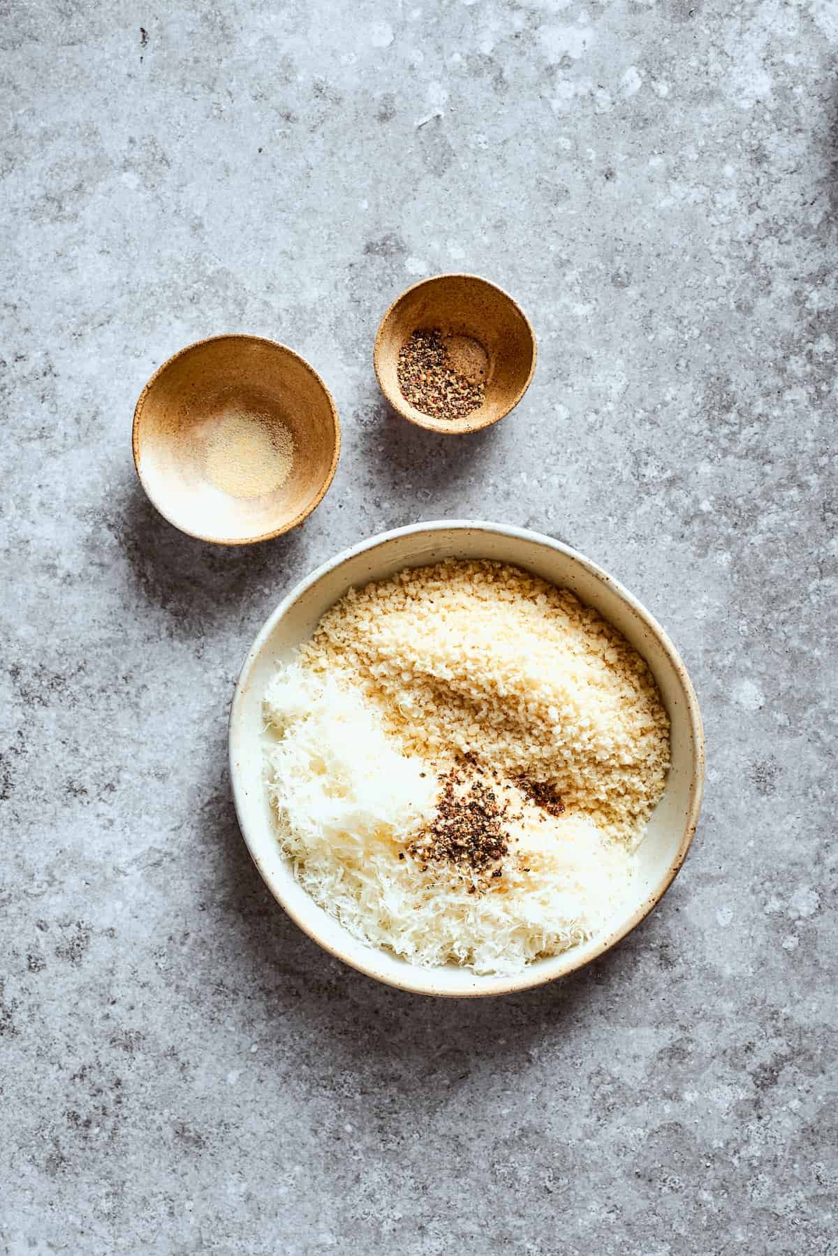 A bowl of breadcrumbs and parmesan next to bowls of seasoning.
