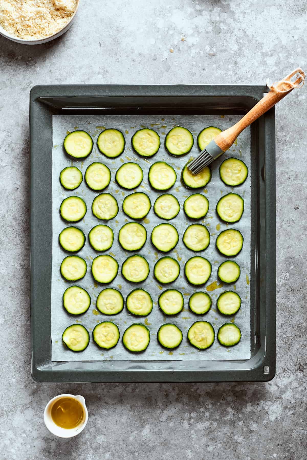 A pastry brush brushes the zucchini chips with oil.