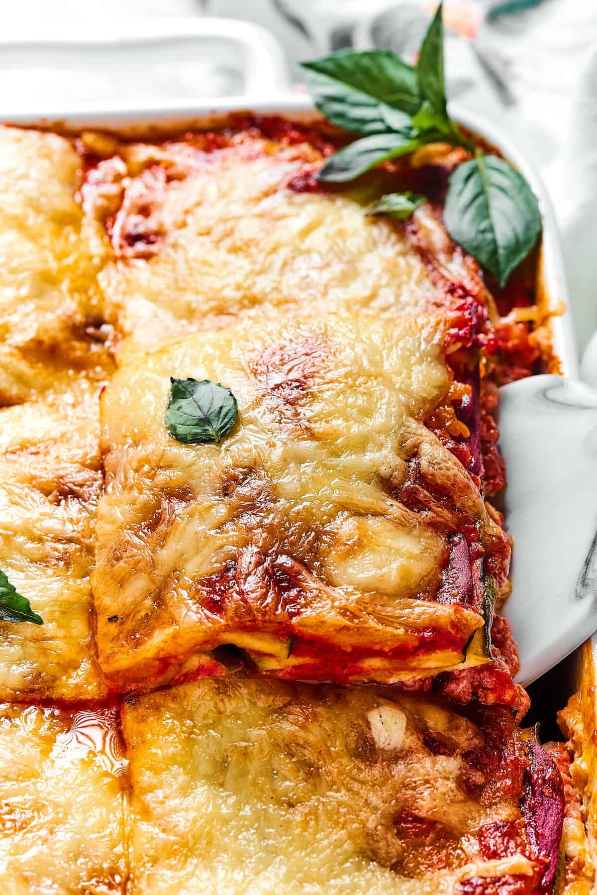 Lasagna being lifted out of a white rectangular baking dish.