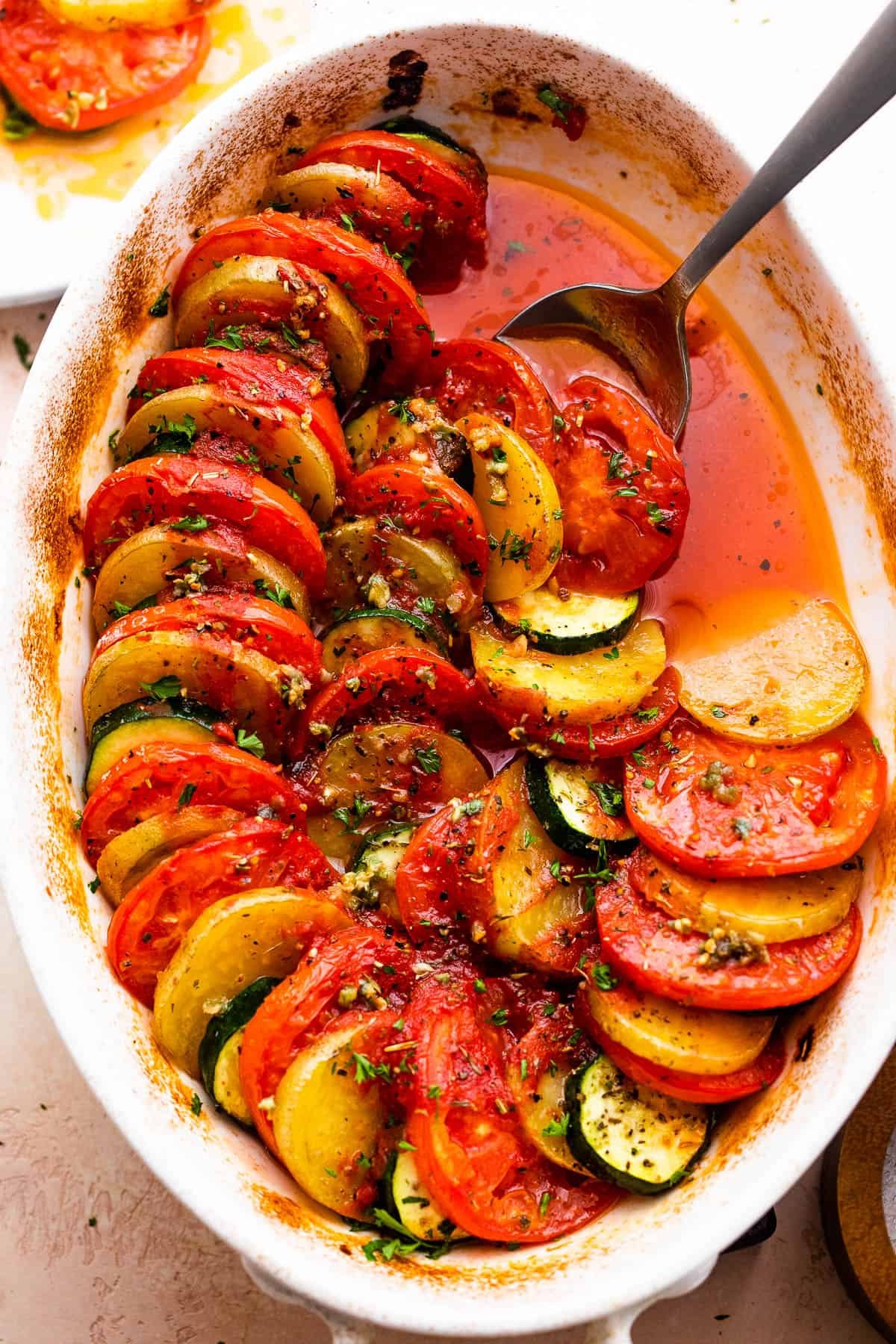 overhead shot of zucchini, tomato, and potato slices arranged accordion style in a baking dish.