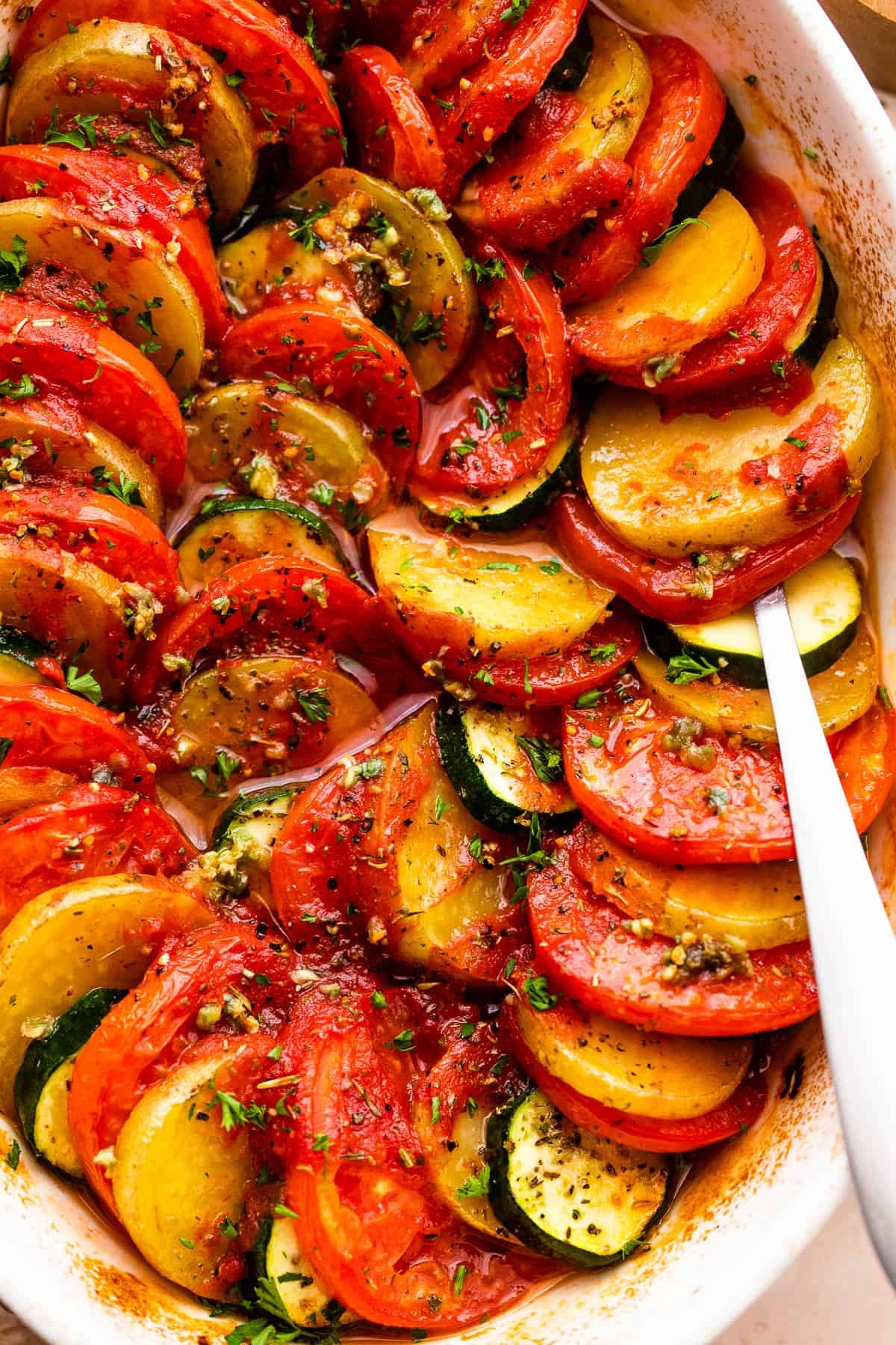 close up shot of zucchini slices, tomato slices, and potato slices arranged accordion style in a baking dish.
