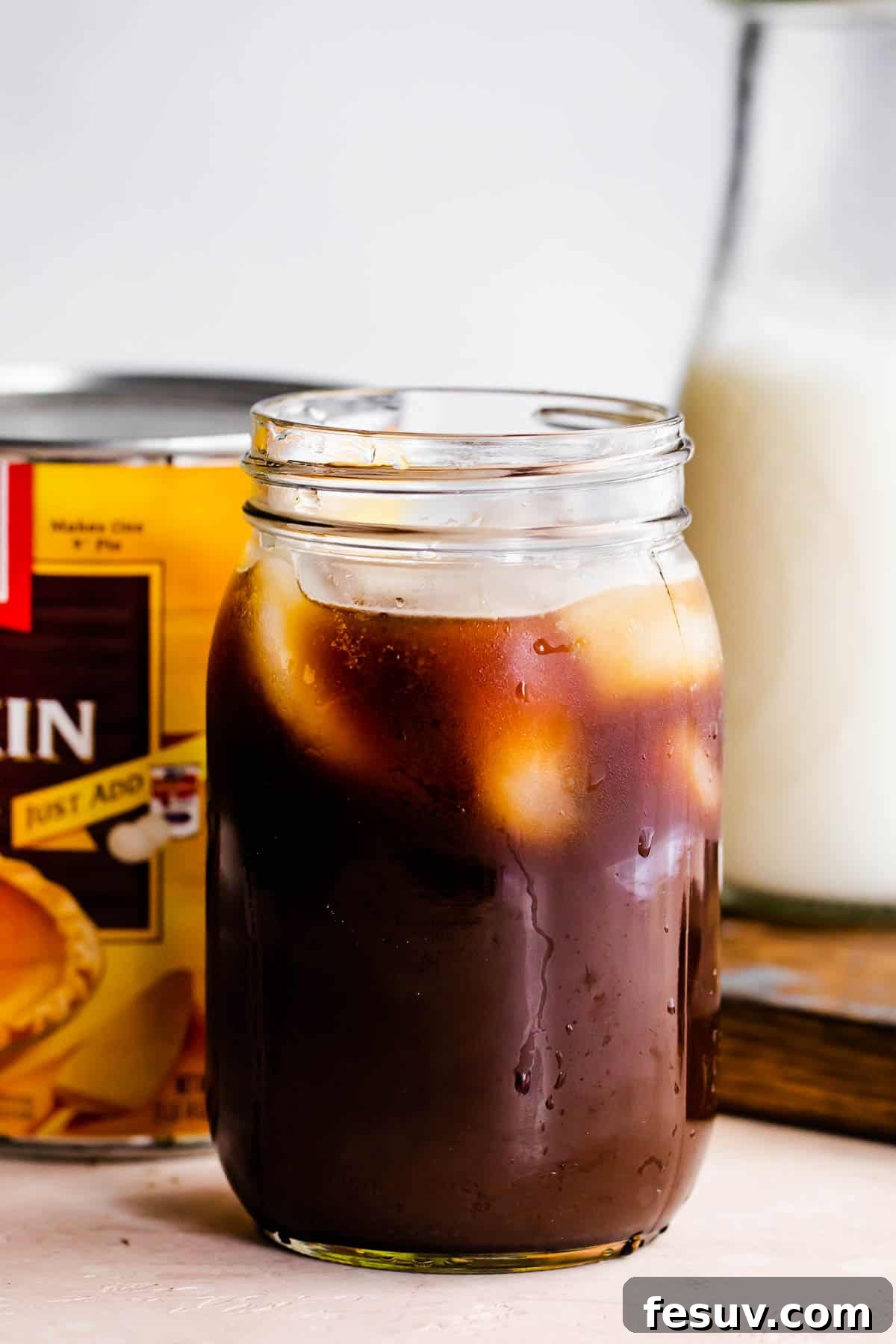 Starbucks Inspired Pumpkin Cream Cold Brew 4 A glass jar filled with coffee and ice, with a can of pumpkin puree behind it.