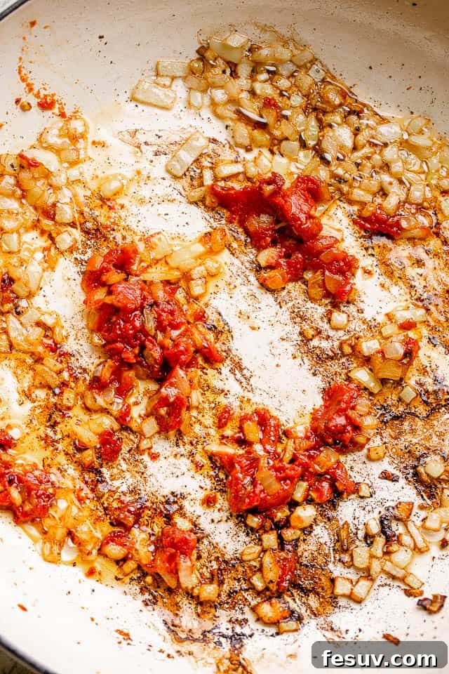 Building flavor: sautéing onions for homemade baked beans, promising sweet, tangy, and spicy notes. Sautéing diced yellow onions in a skillet with rendered bacon grease, building the flavor base for the baked beans.