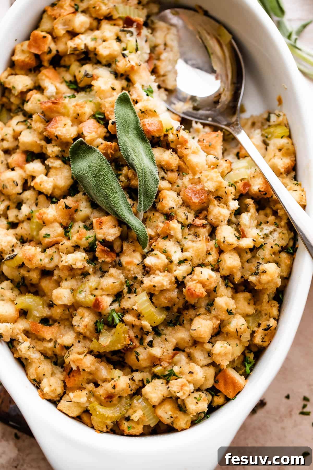 overhead shot of fresh baked stuffing (dressing) sprinkled with sage leaves and herbs in a white dish.