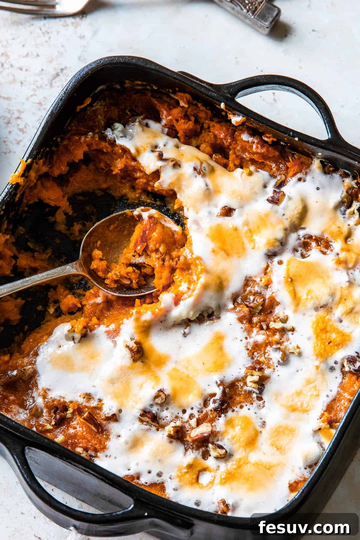 Sweet potato casserole with a spoon scooping out a portion, showcasing melted marshmallows and pecans.