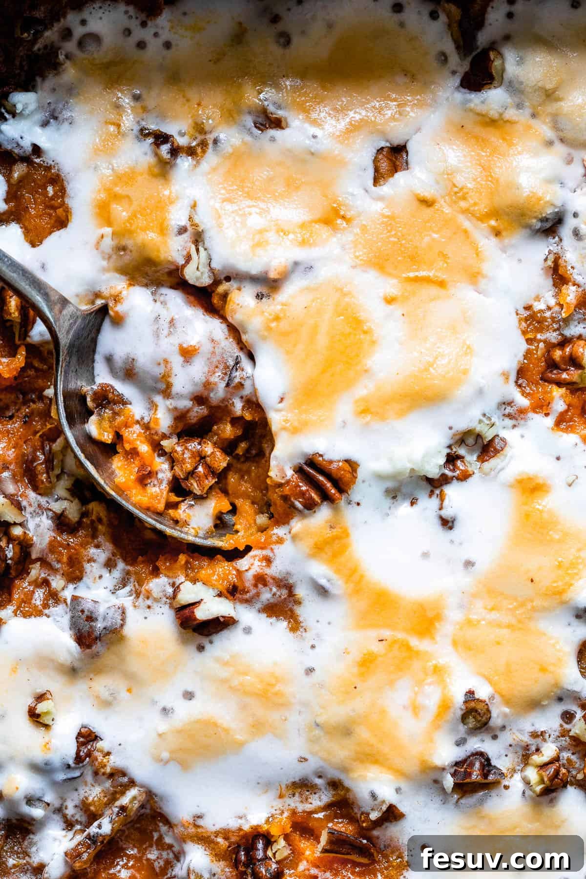 A close-up of a sweet potato casserole, revealing its creamy texture before baking, topped with pecans and mini marshmallows.