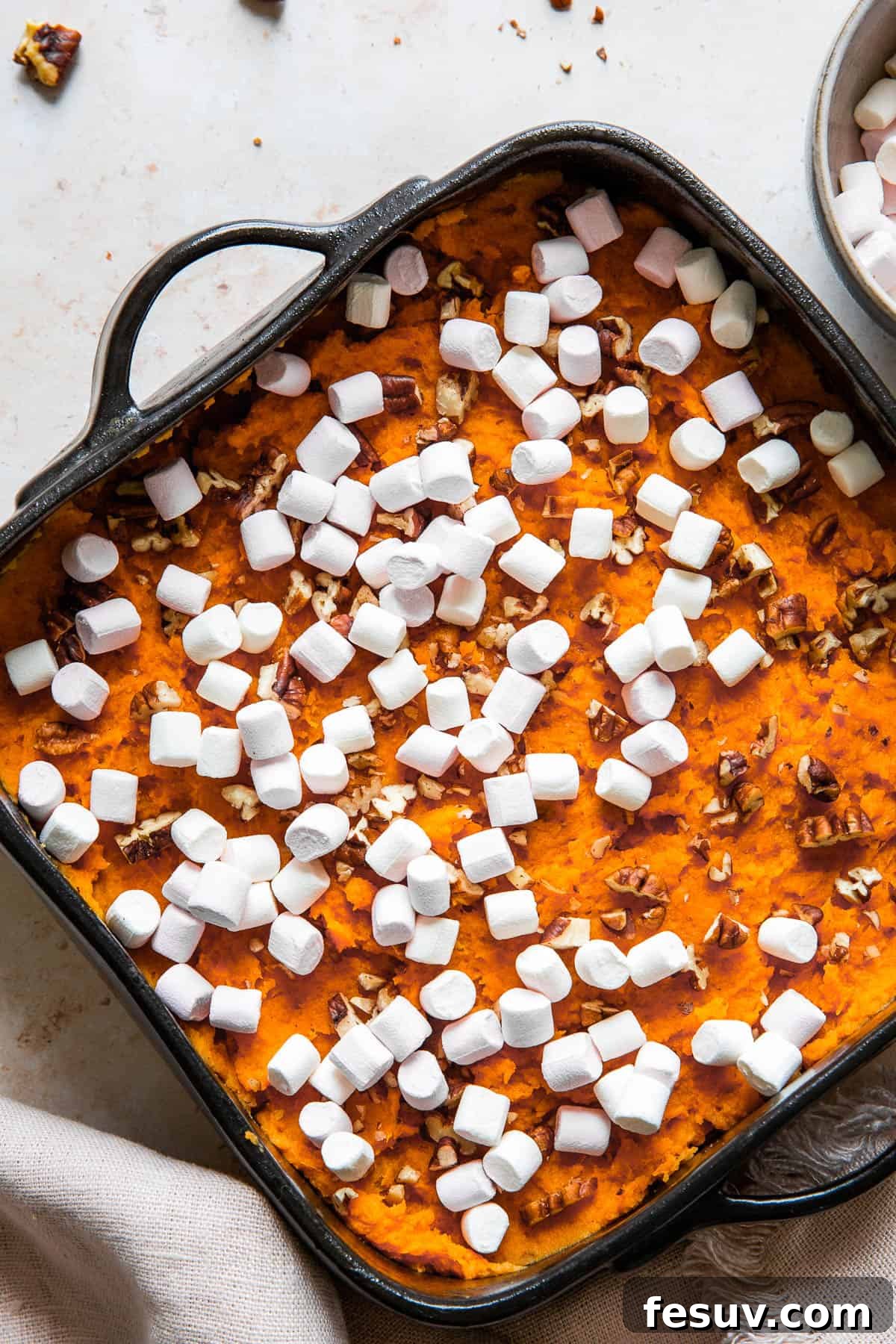 Close up shot of an unbaked sweet potato casserole, generously sprinkled with chopped pecans and mini marshmallows, ready for the oven.