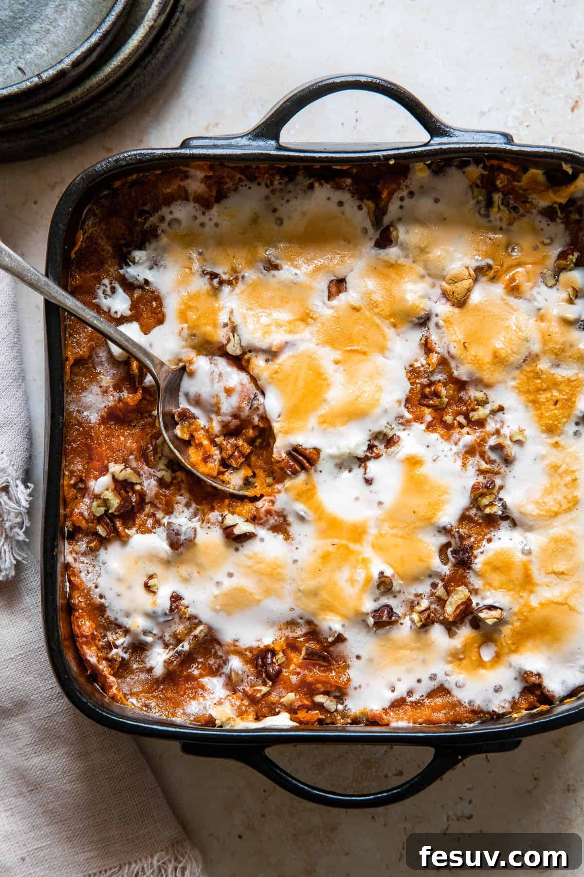 A serving spoon resting in a square black baking dish of sweet potato casserole, ready to be enjoyed.